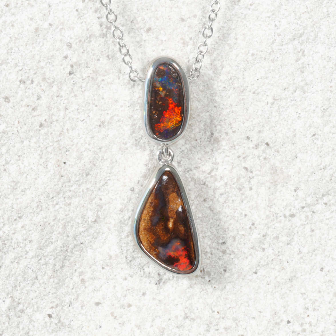 Necklace with a pendant featuring two teardrop-shaped opal stones on a textured white background