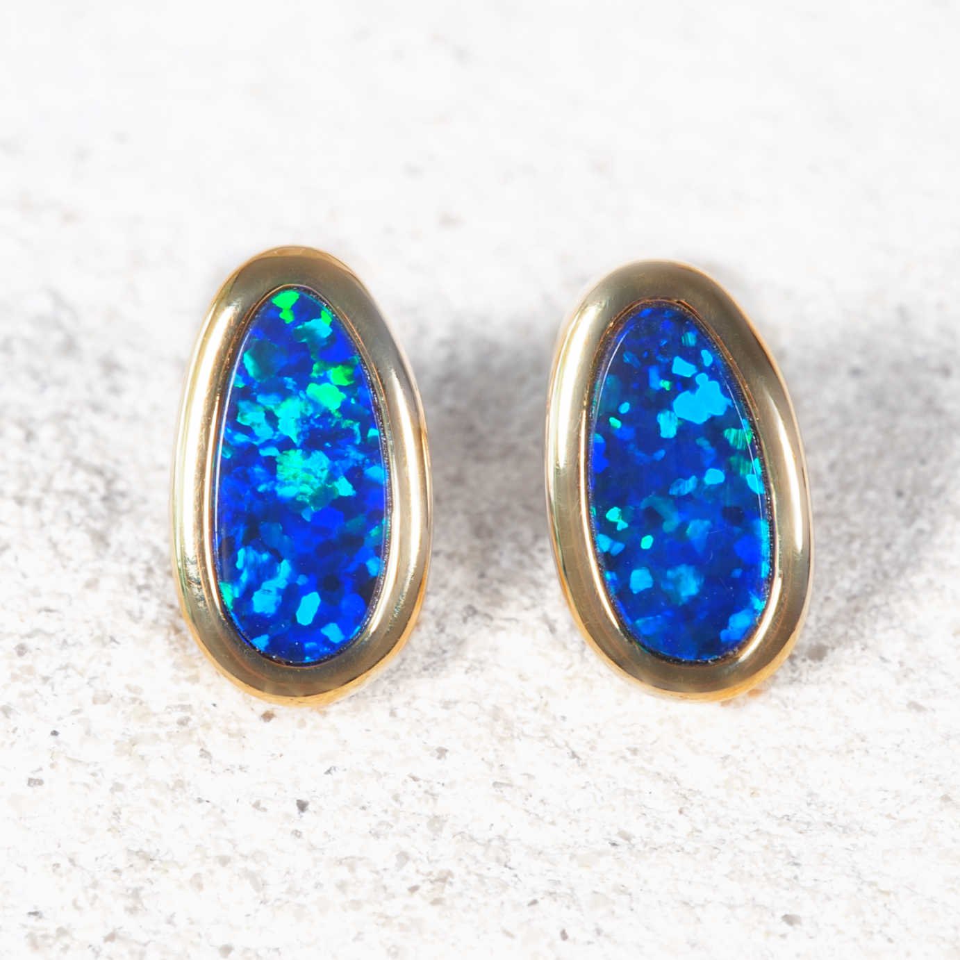 Pair of blue opal earrings with gold settings on a textured white surface
