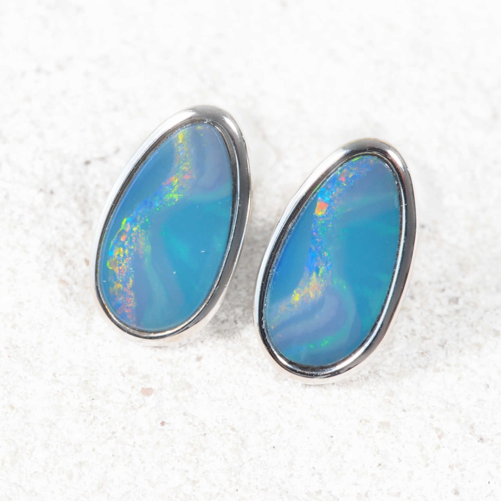 Opal earrings with silver setting on a textured white background