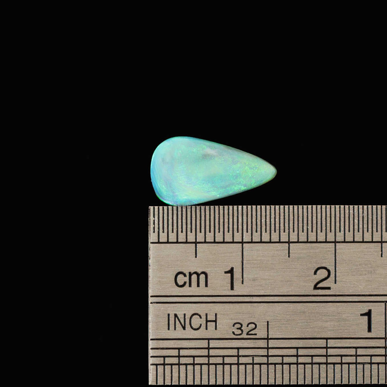 Lightning Ridge black opal stone next to a ruler on a black background