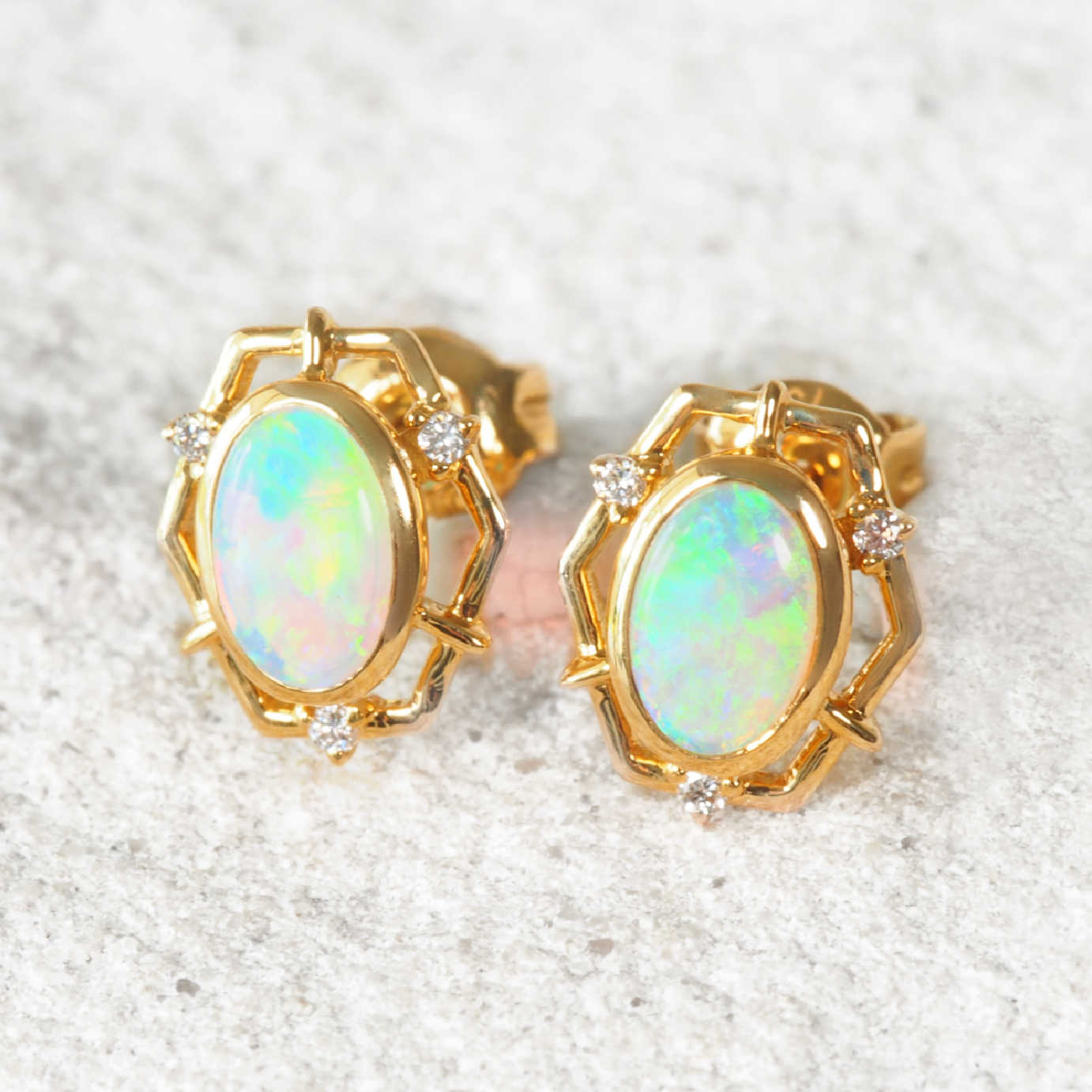 Gold earrings with green Australian opal stones on a textured white background