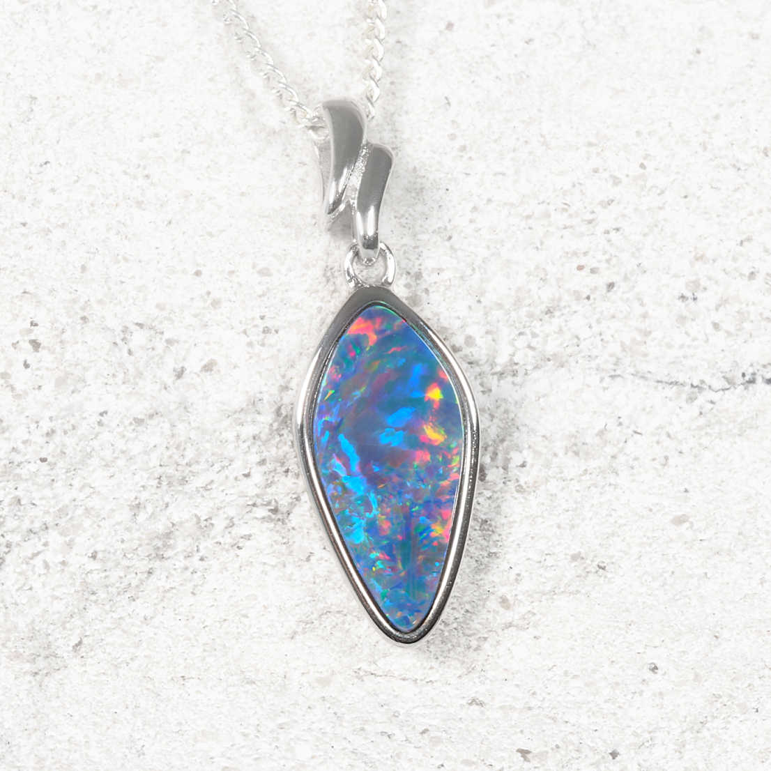 A silver opal necklace featuring a teardrop-shaped opal gemstone with vibrant blue, orange, and purple flashes, set on a textured light gray background.