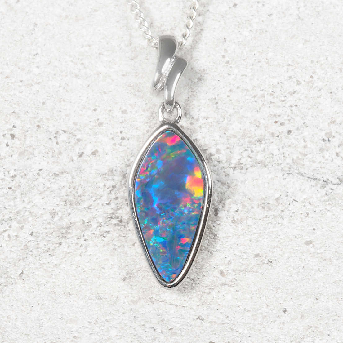 A silver opal pendant necklace featuring a teardrop-shaped opal gemstone with vibrant blue, pink, and orange flashes, displayed on a textured light gray background.