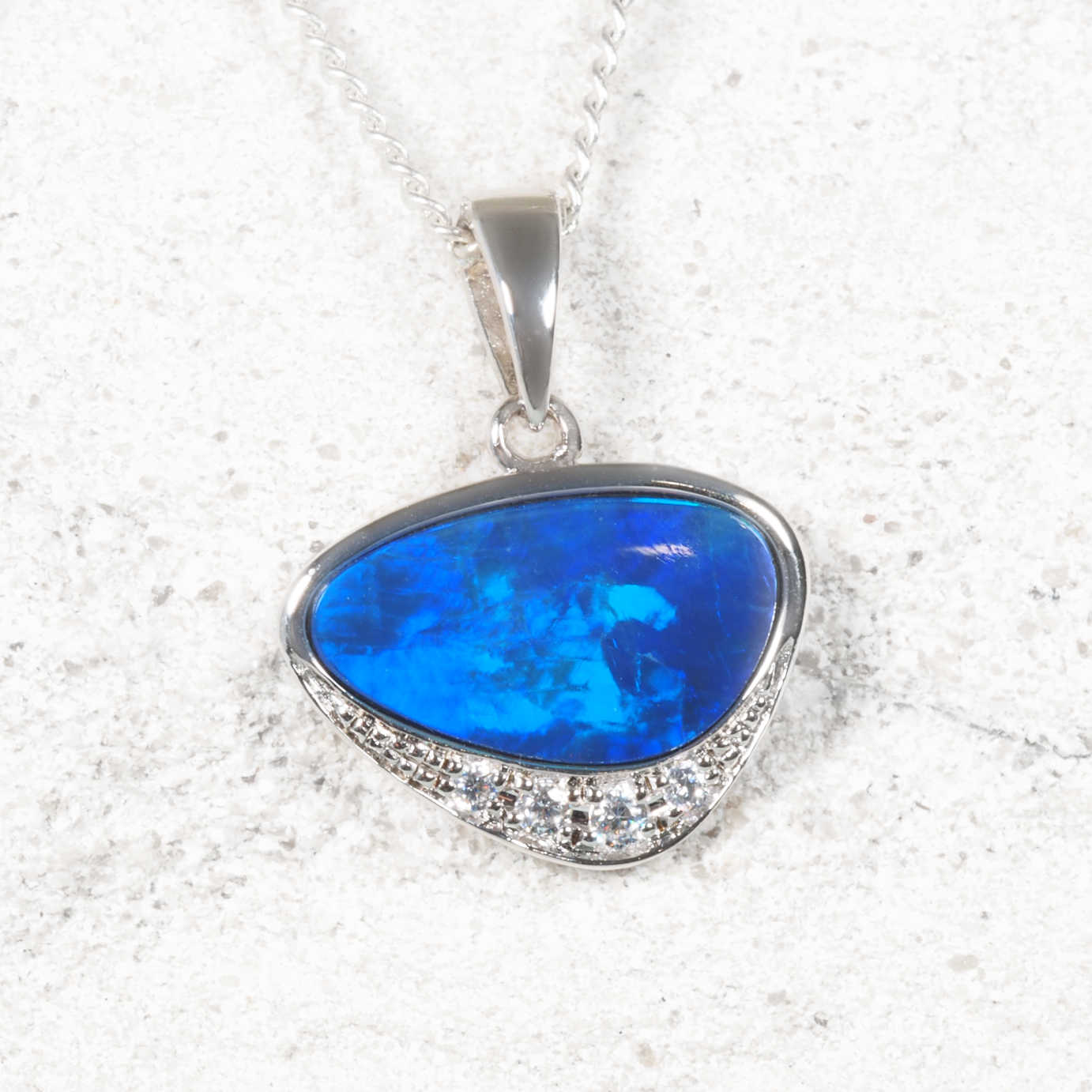 Blue opal pendant with a silver chain on a textured white background