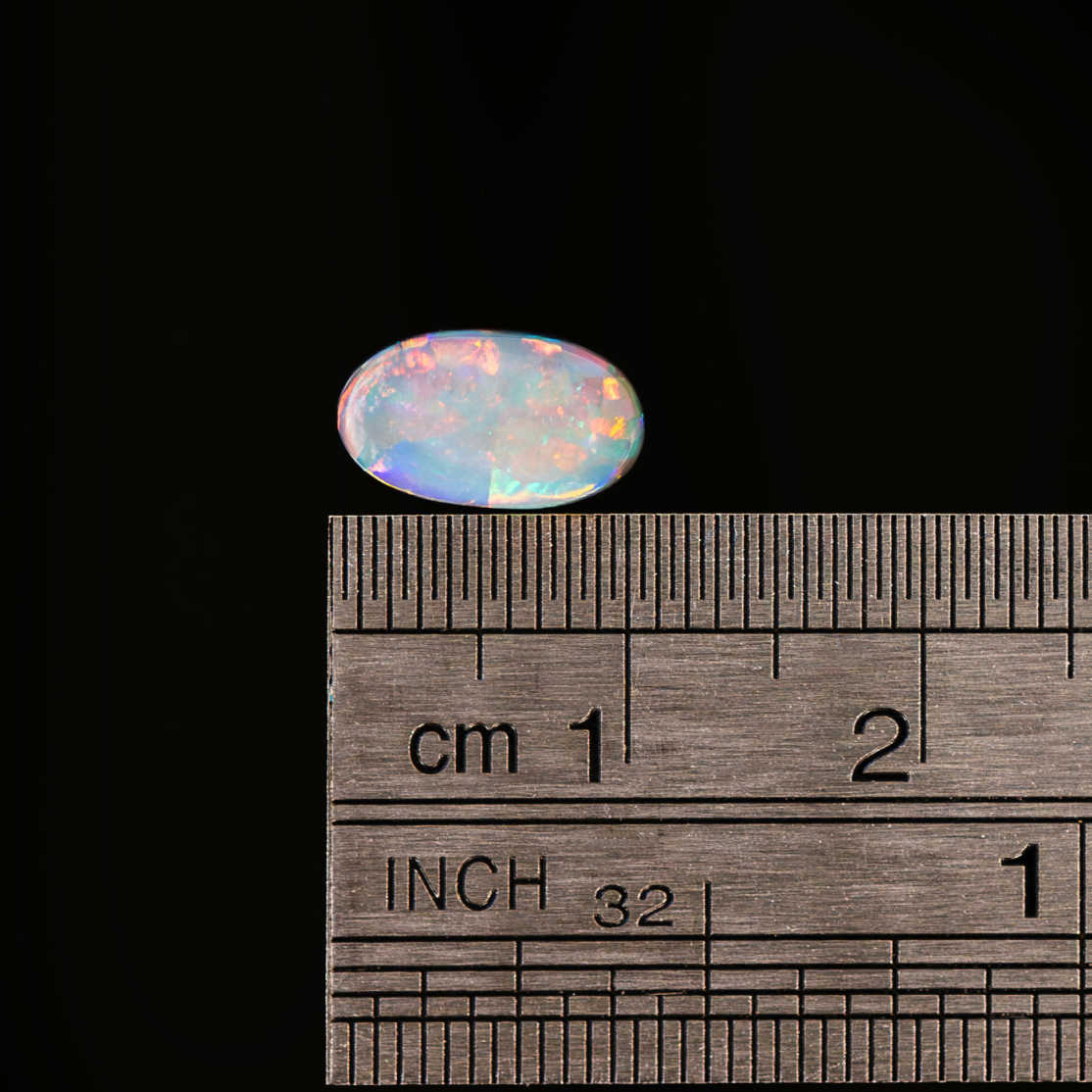 Opal stone next to a ruler for size measurement on a black background