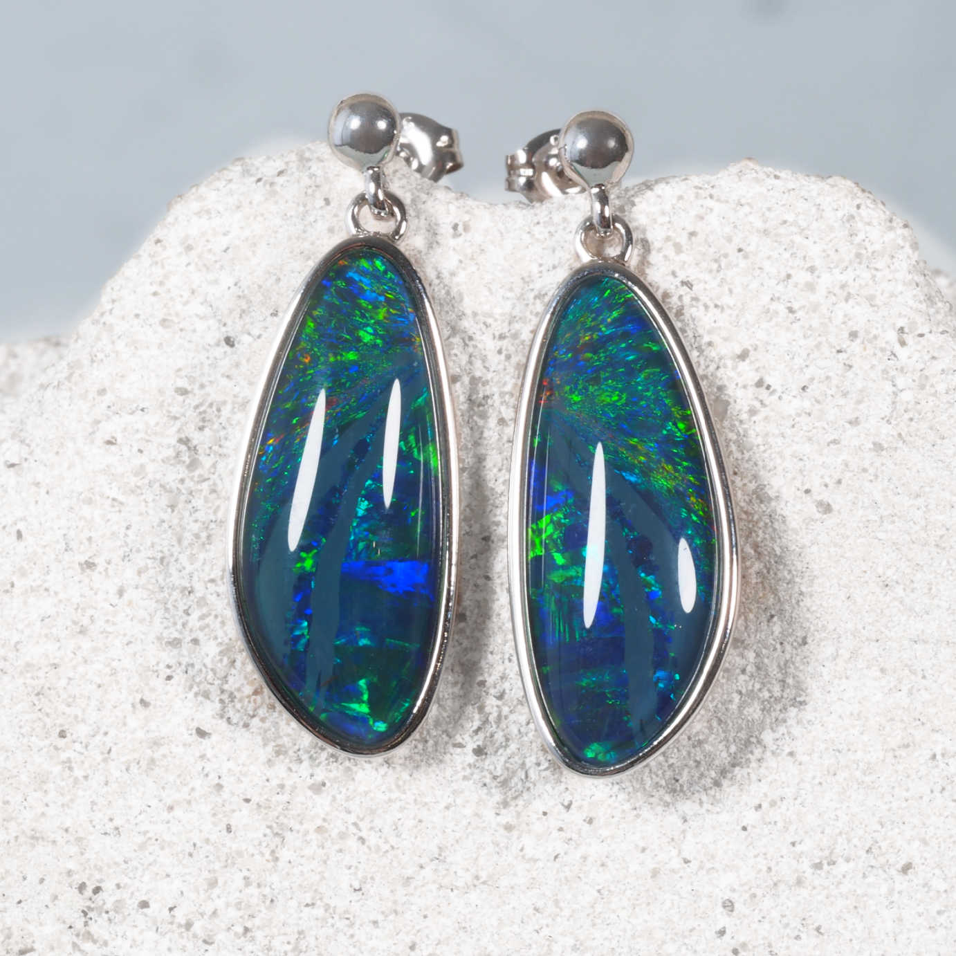 Opal earrings with silver setting on a textured surface
