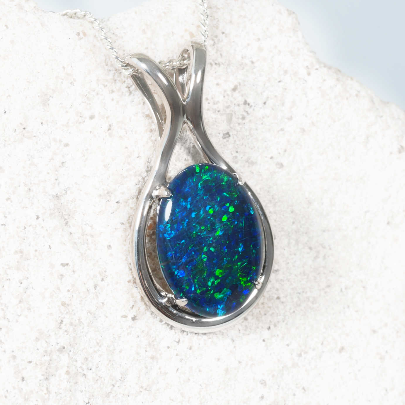 Blue opal pendant in a silver setting on a white rock background