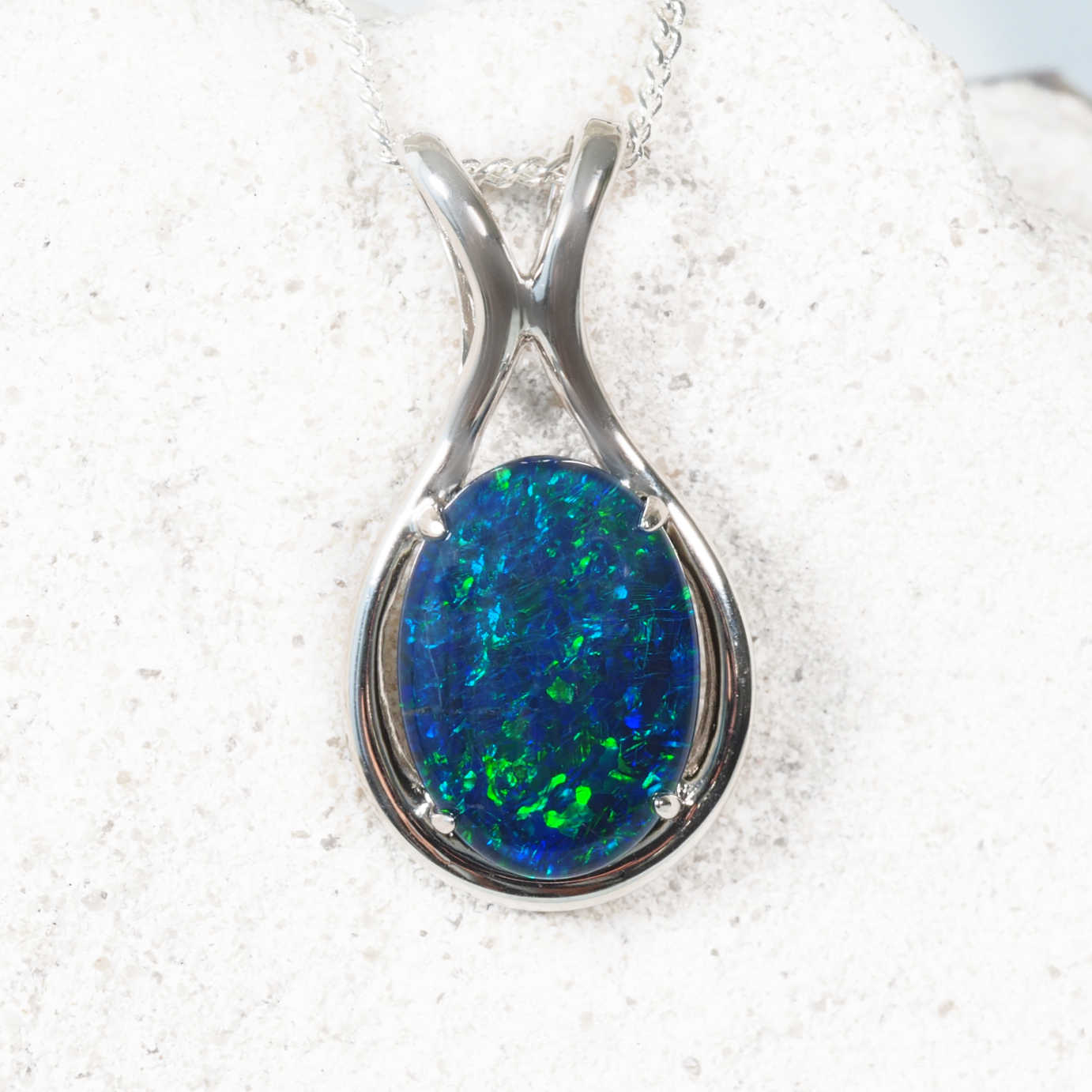 Opal pendant in a silver setting on a white sandy background