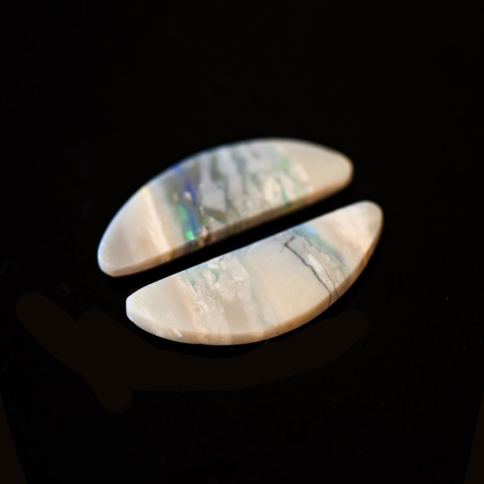 Two Lightning Ridge opal stones with iridescent patterns on a black background