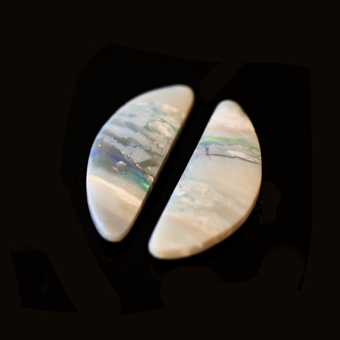 Two solid opal stones with a scenic landscape pattern on a black background