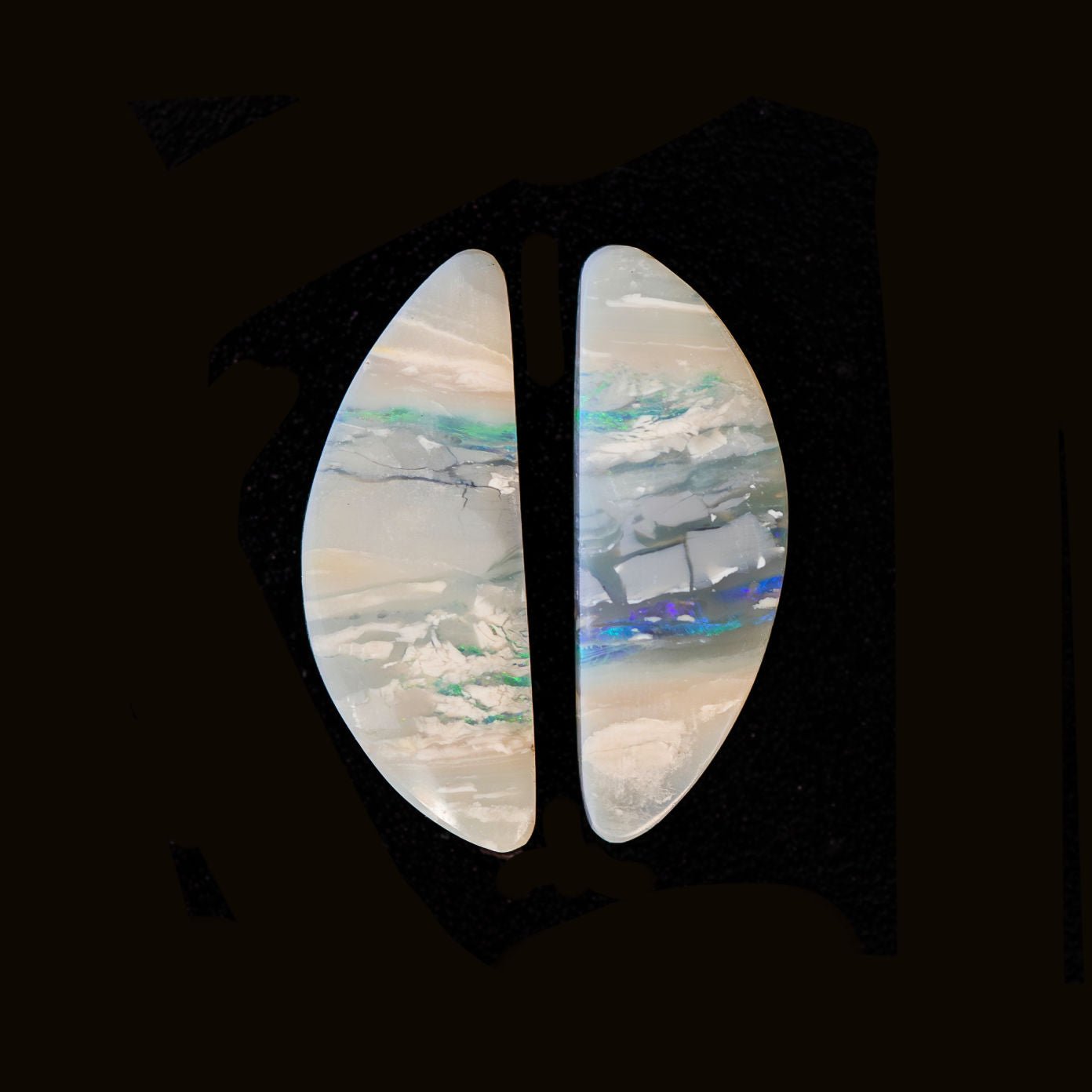 Two white opals with green and blue colours running through on a dark background