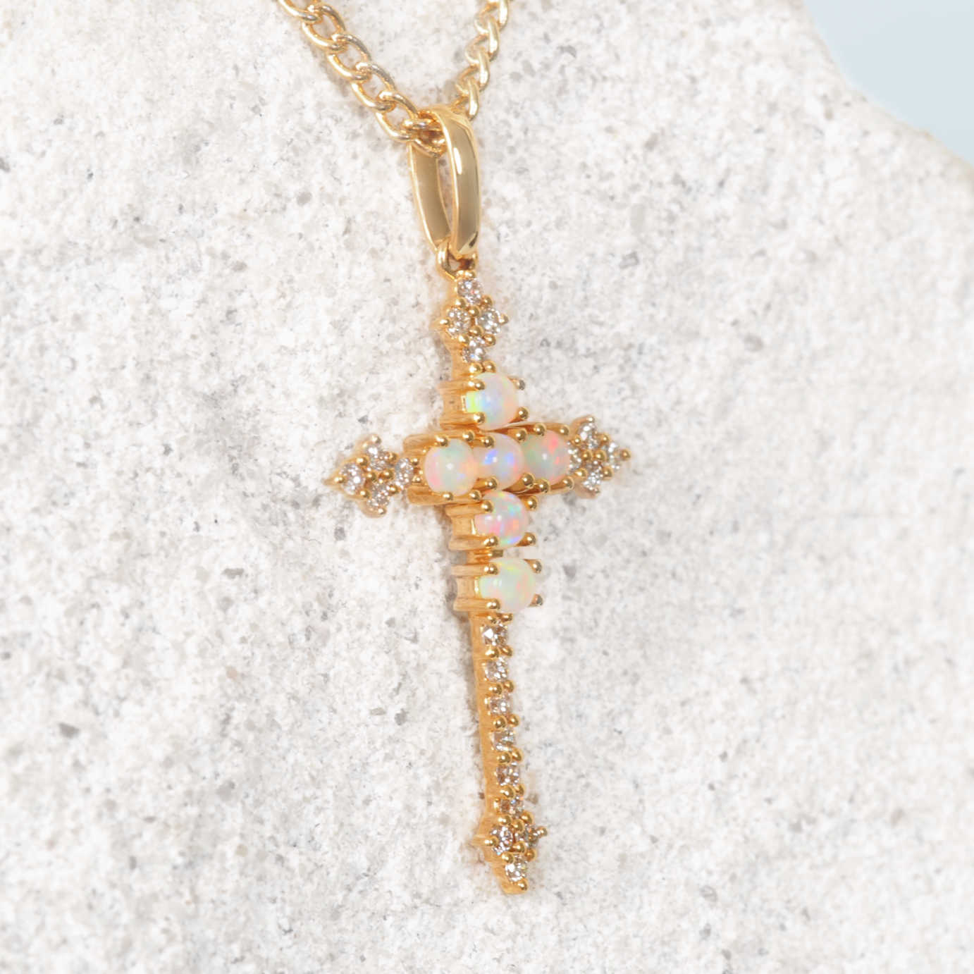 Gold opal cross pendant with real Coober Pedy opal stones on a textured white surface
