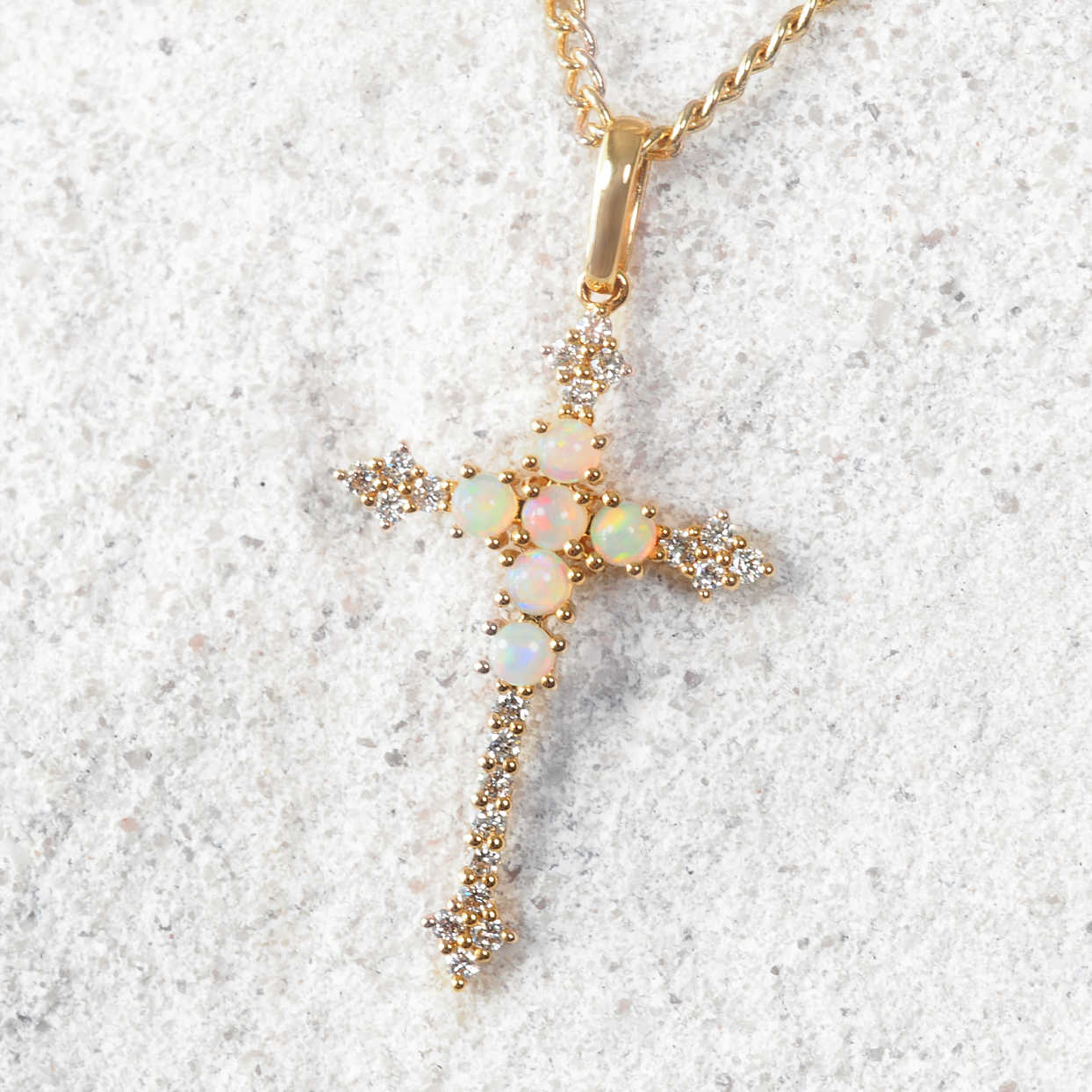 Gold cross pendant with opal stones on a white background