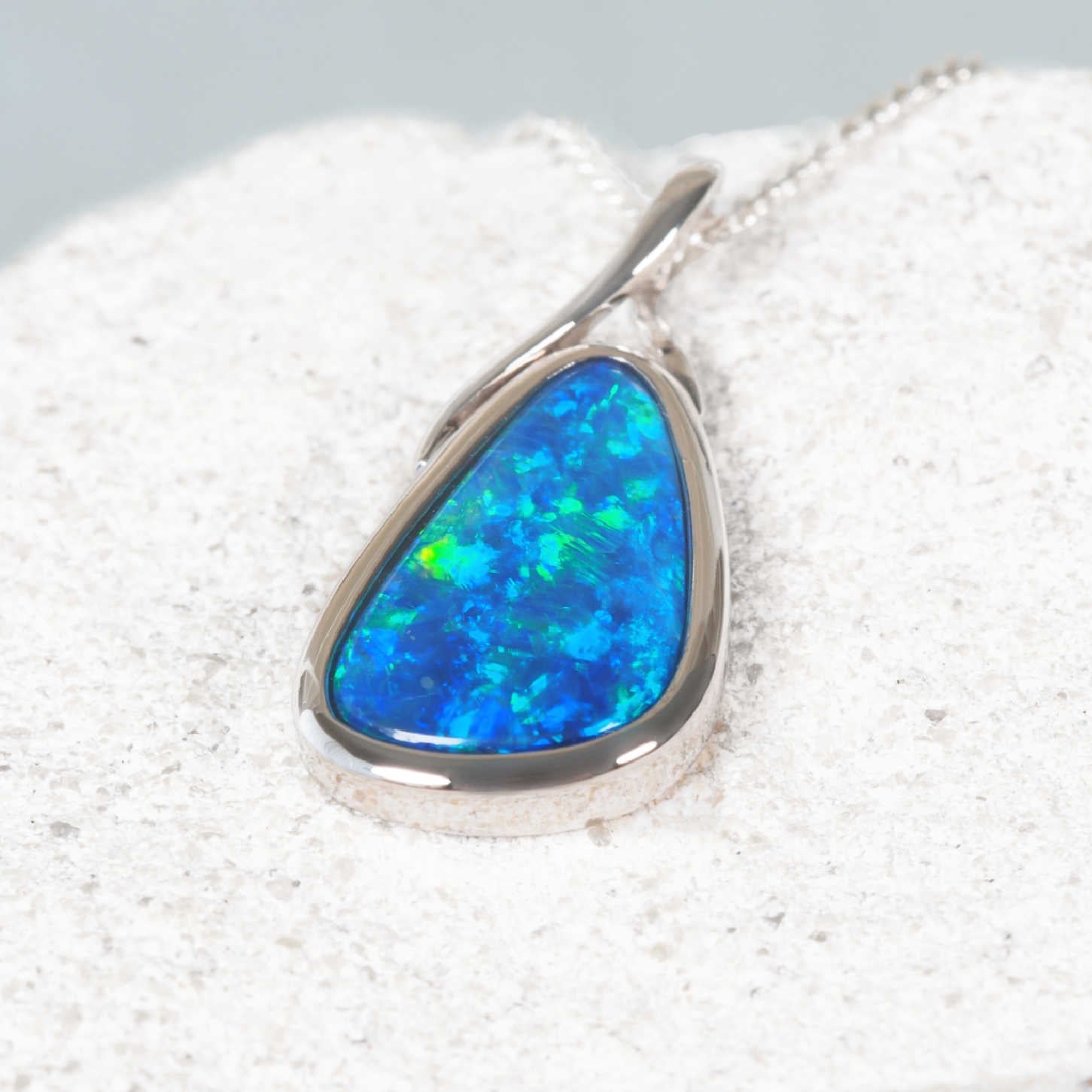 White gold opal pendant on a textured white surface