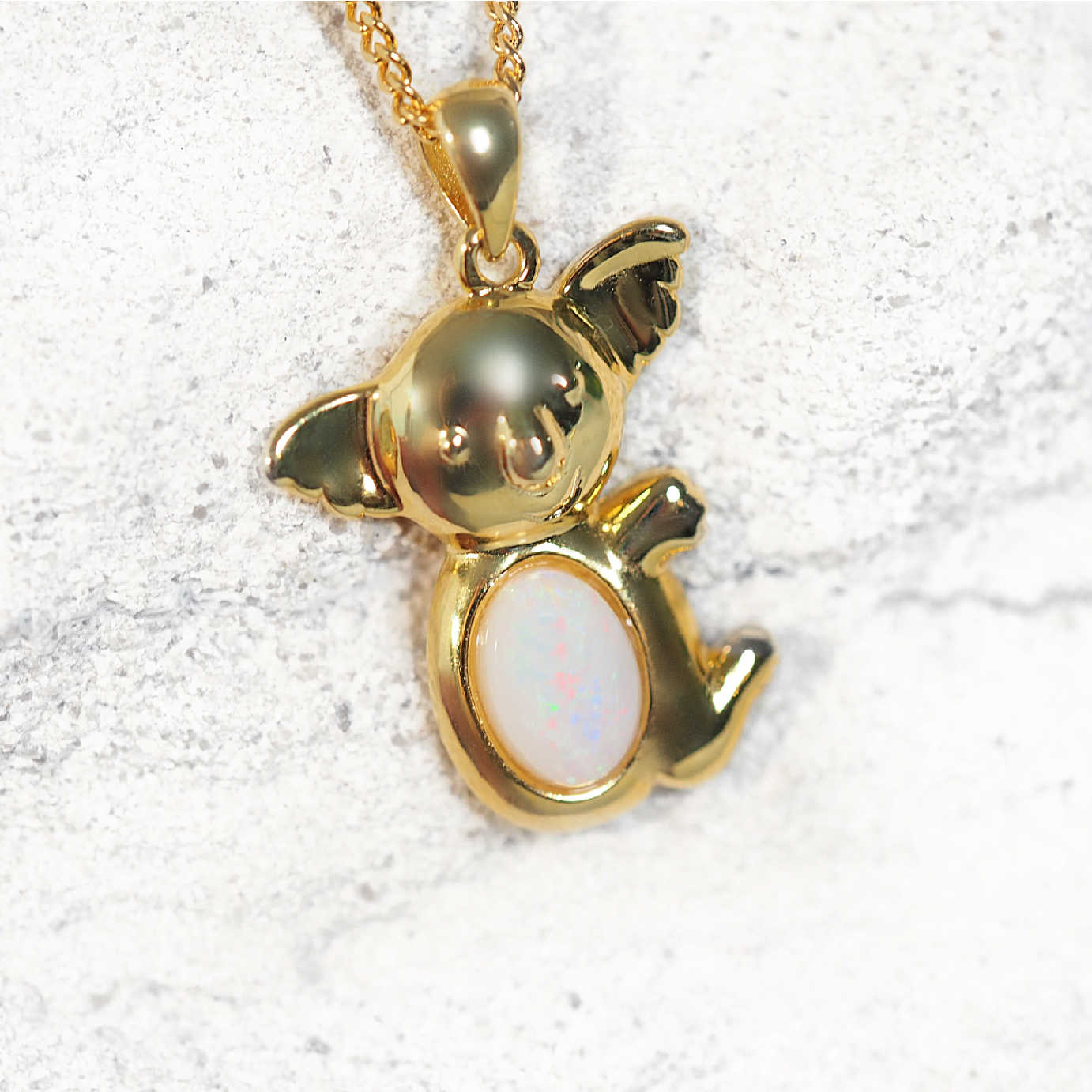 Gold koala opal pendant with a white stone on a textured white background