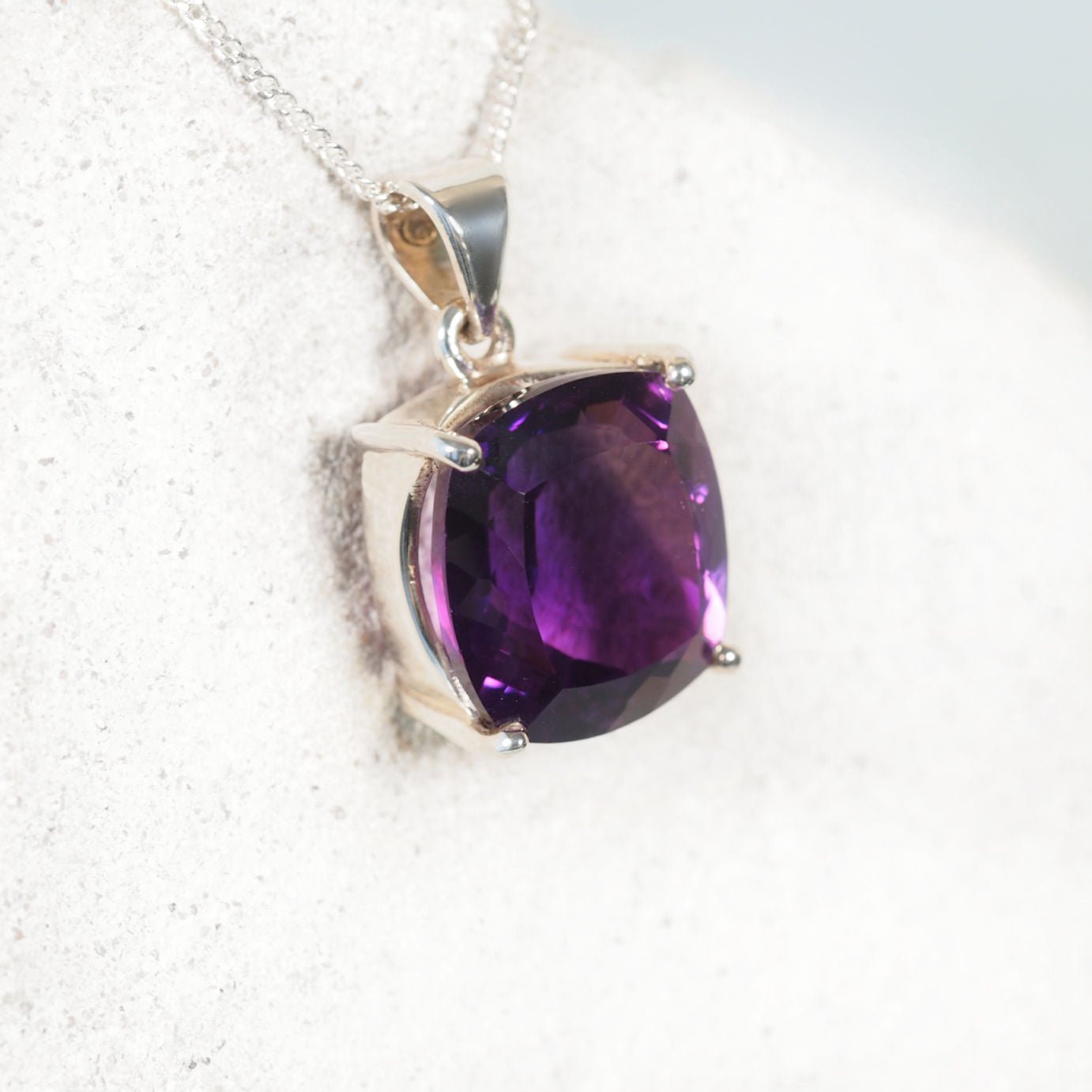 Amethyst pendant on a silver chain against a white background
