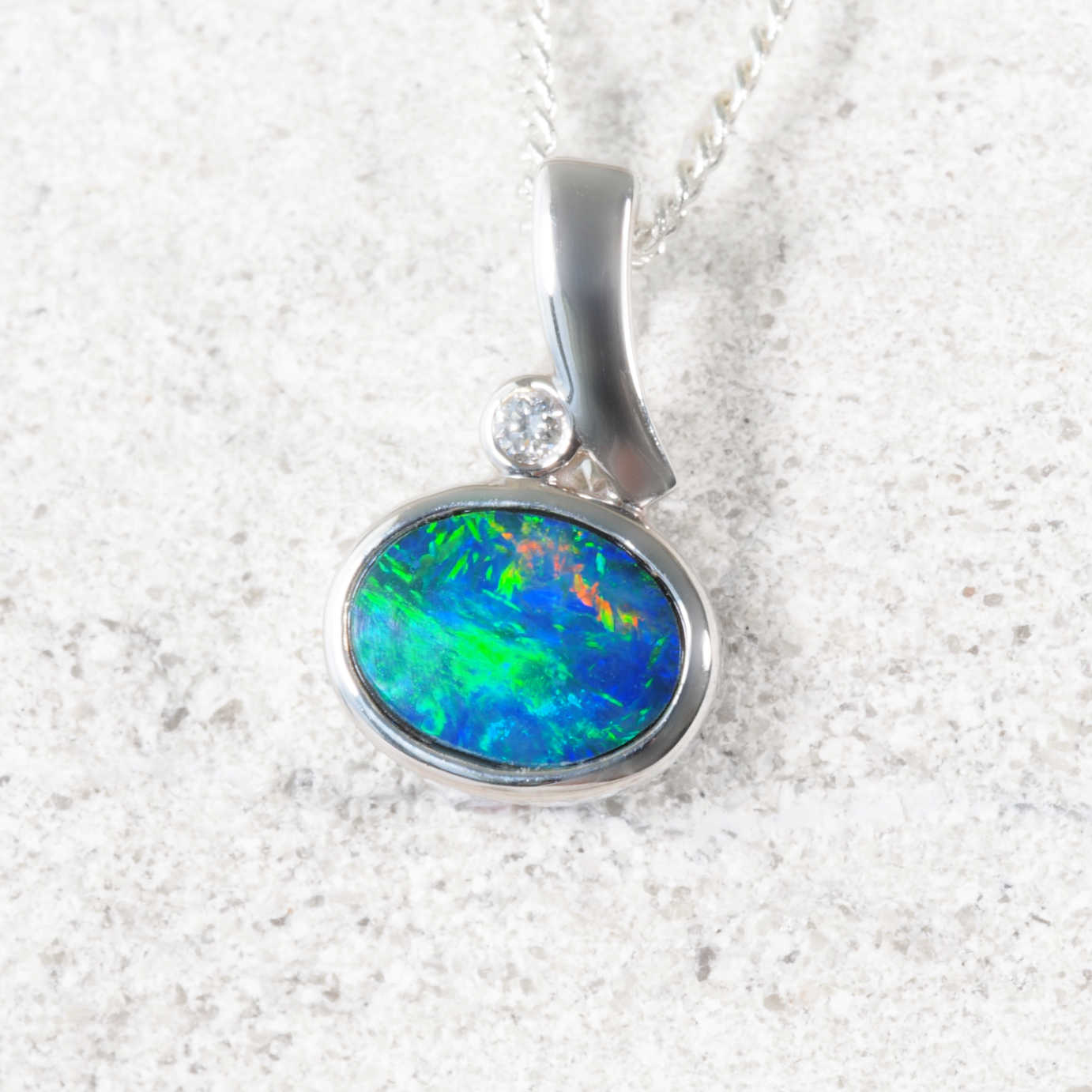 Doublet opal pendant with white gold setting on a textured white background