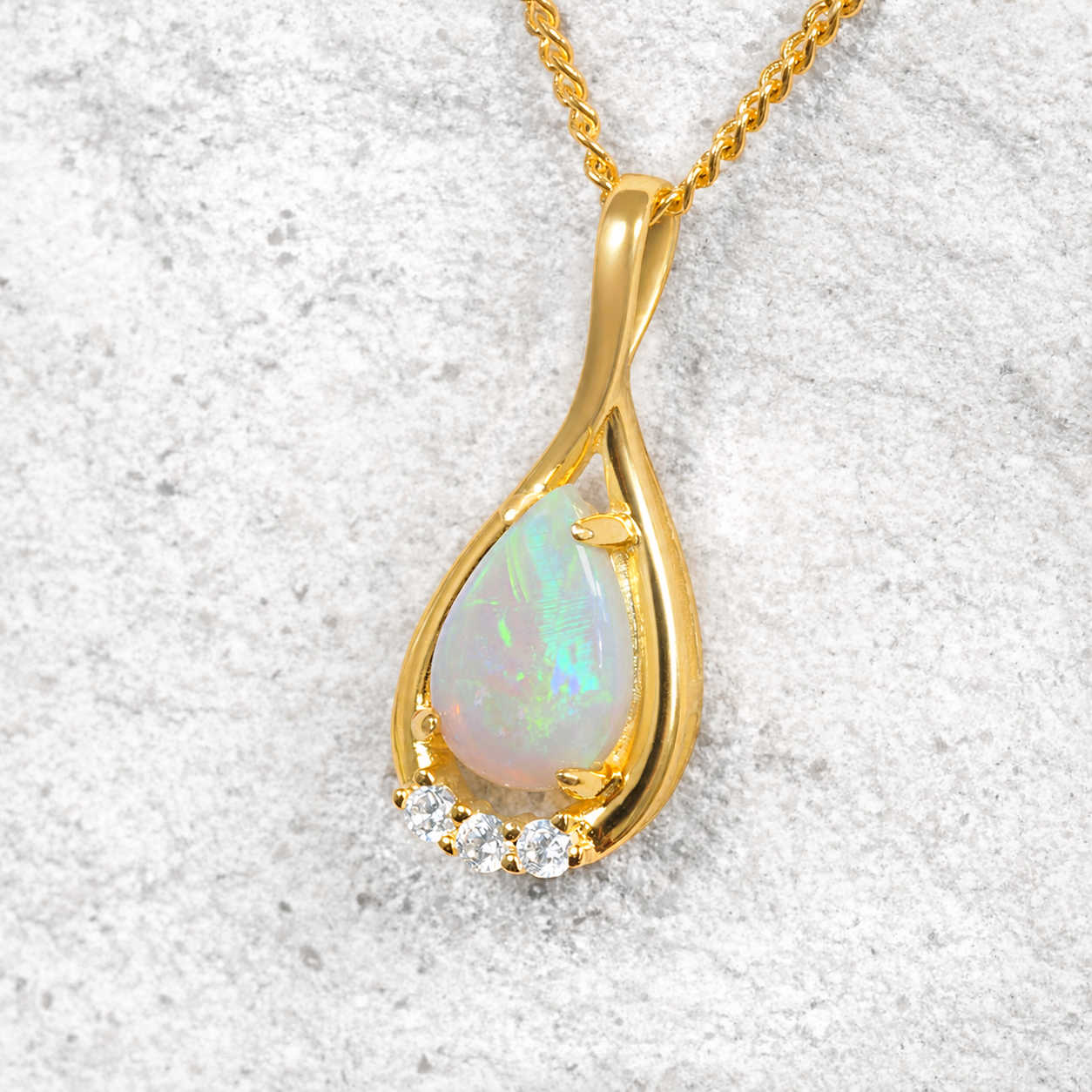 Gold pendant with a teardrop-shaped opal stone on a textured white background