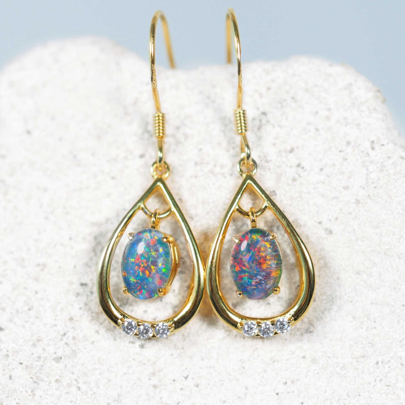 Gold teardrop earrings with opal stones on a white background