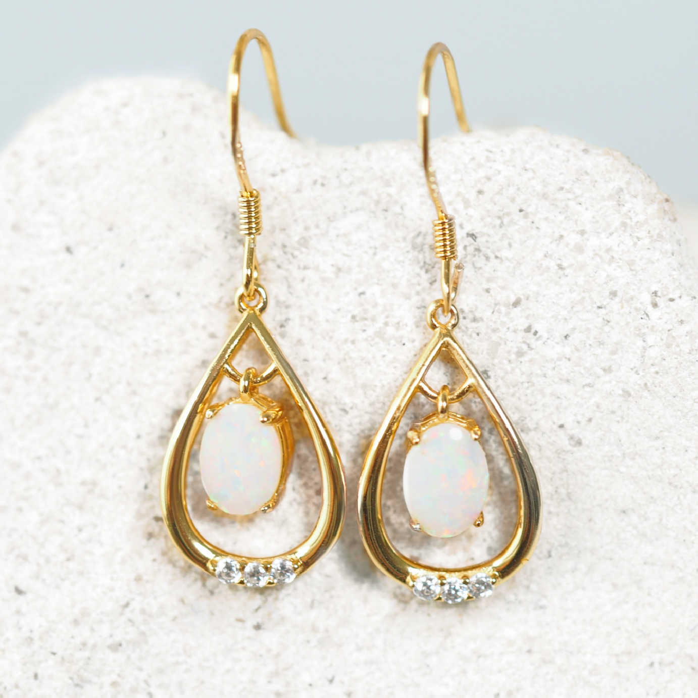 Gold teardrop opal earrings with white stones on a textured white surface