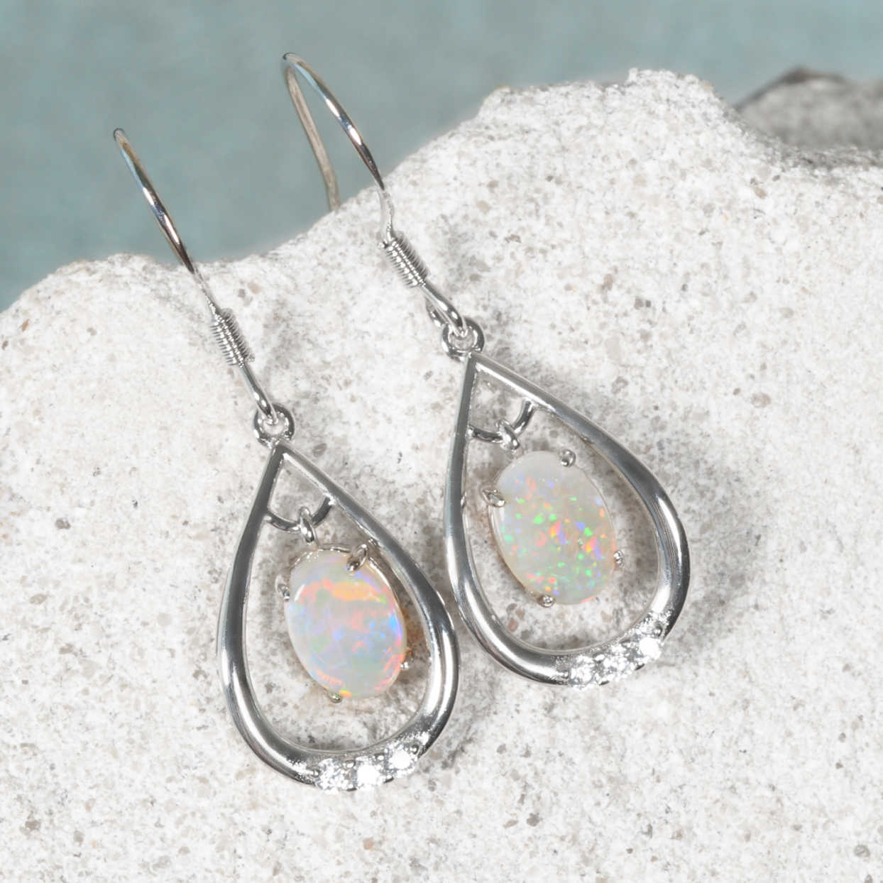 Oval-shaped opal earrings on a textured surface with a neutral background