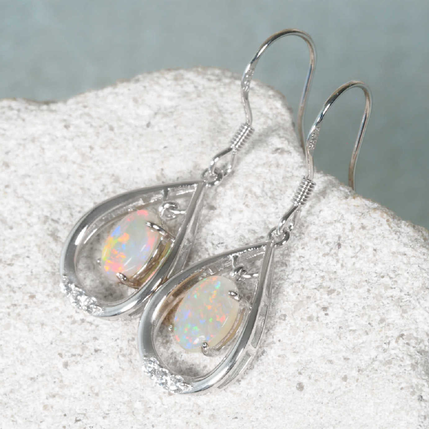 Silver teardrop earrings with opal stones on a textured surface