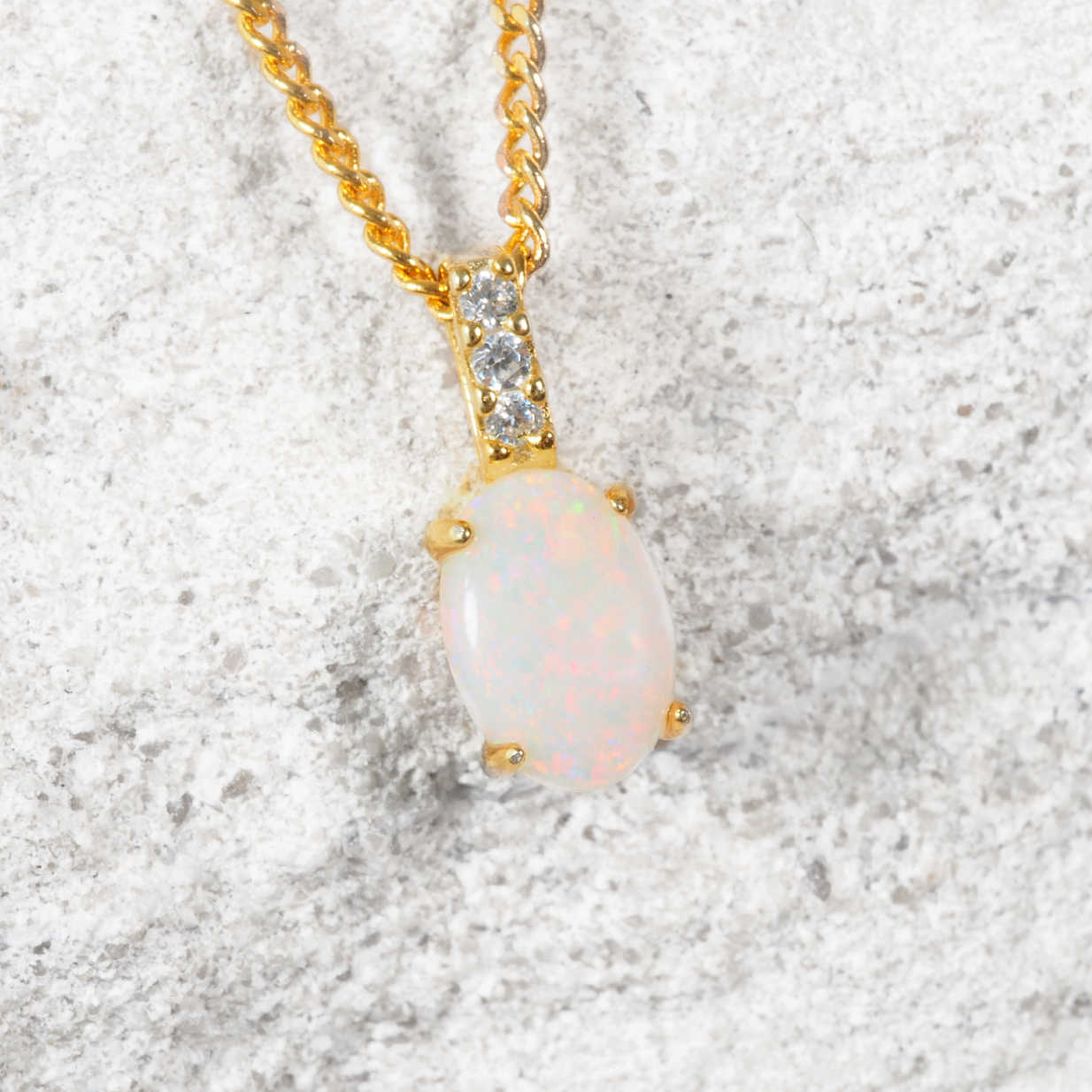 Opal pendant necklace with gold chain on a textured gray background