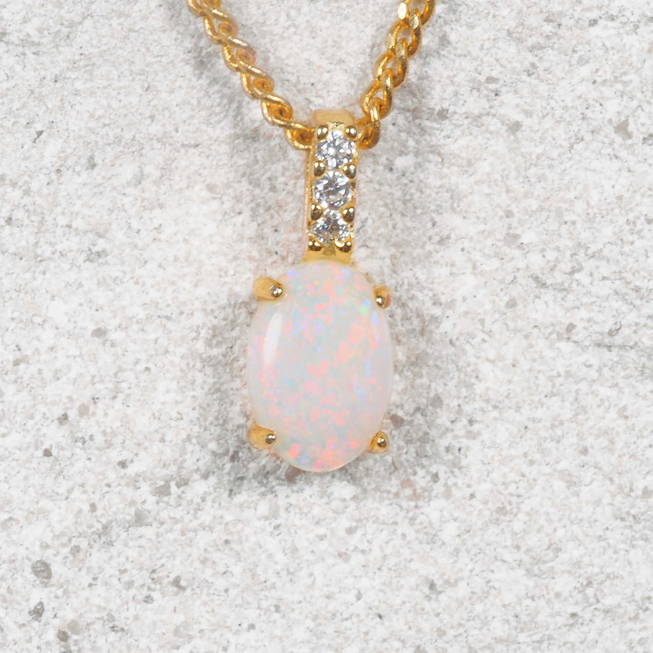 Opal pendant necklace with gold chain on a textured surface