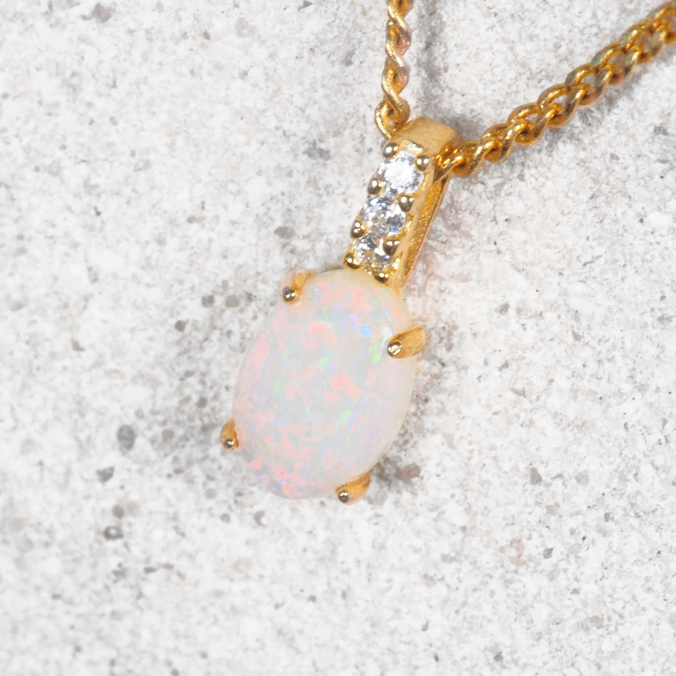 White opal pendant necklace with gold chain on a textured surface