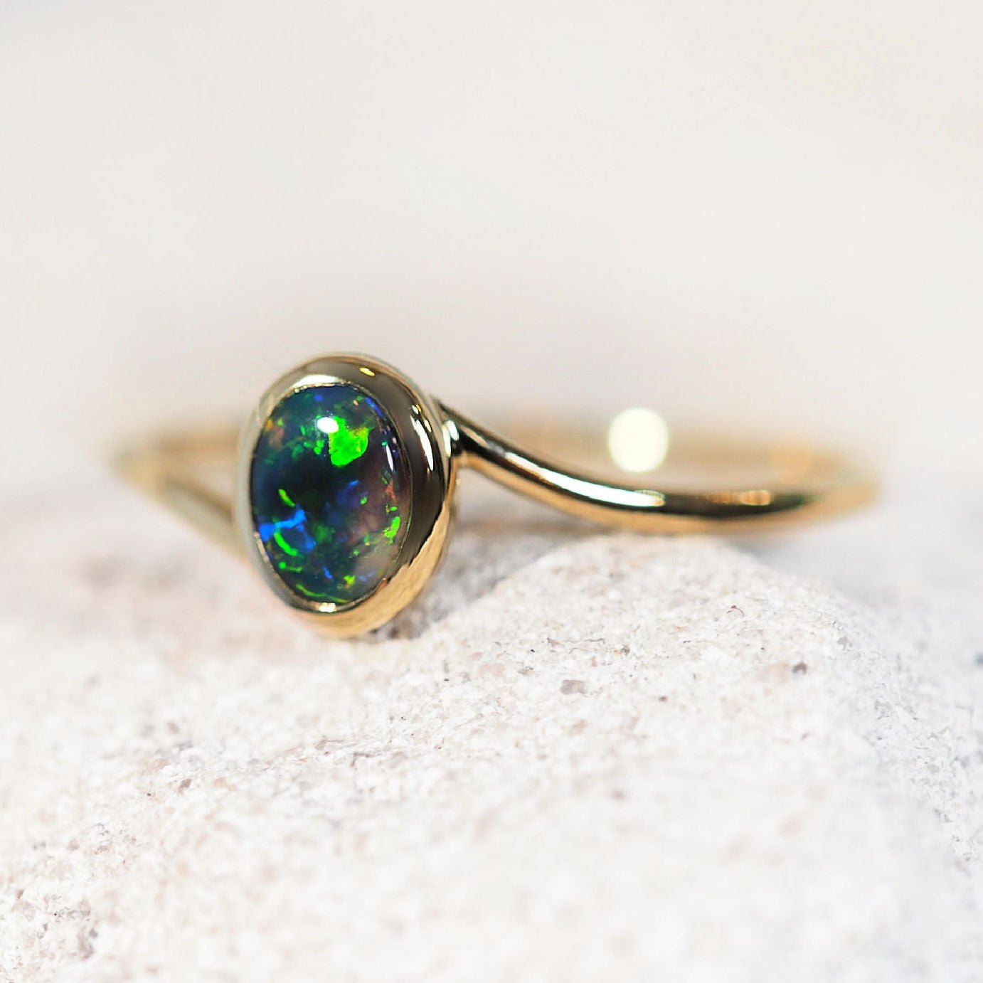 Gold ring with a green Lightning Ridge opal stone on a light background