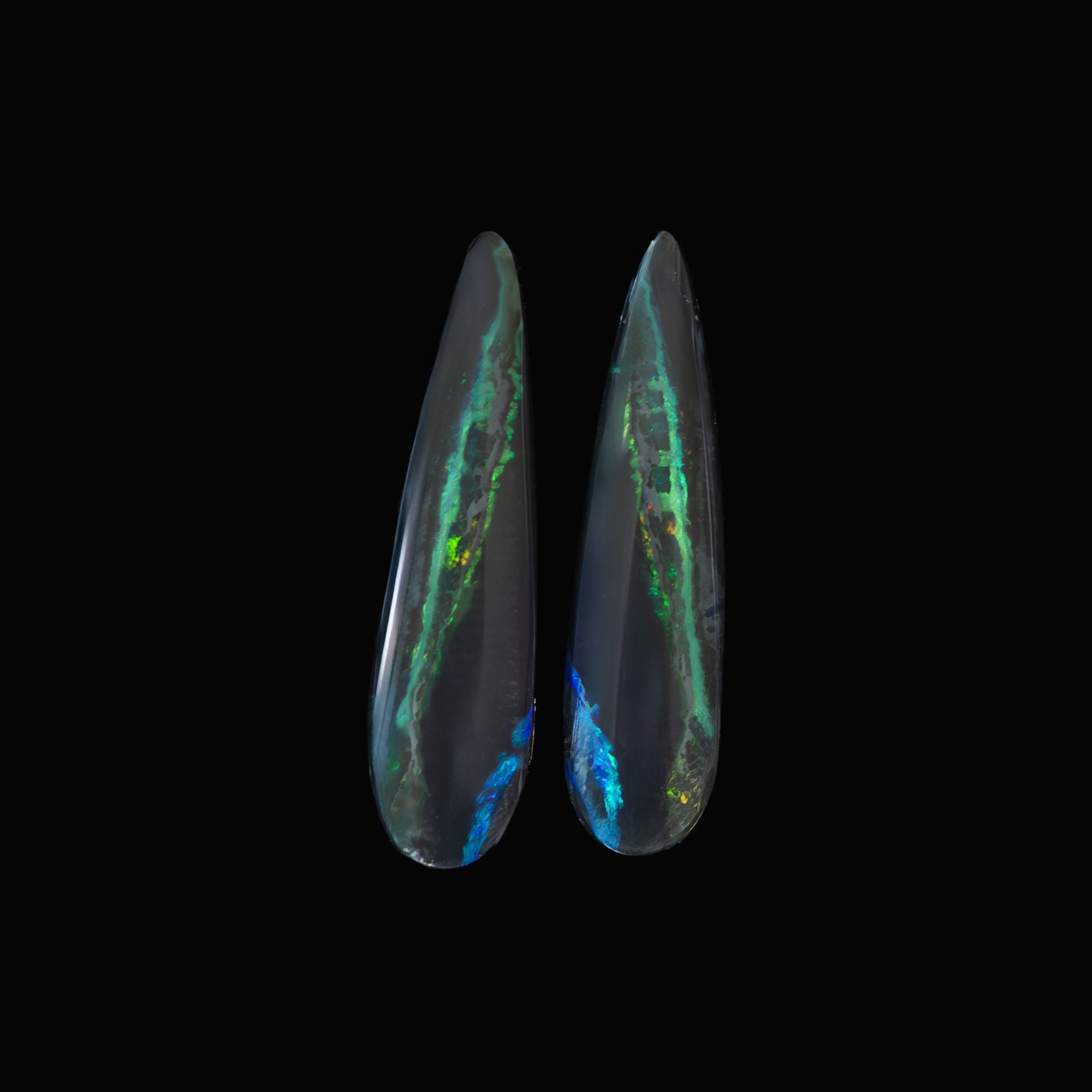 Two black opal stones with colorful inclusions on a black background