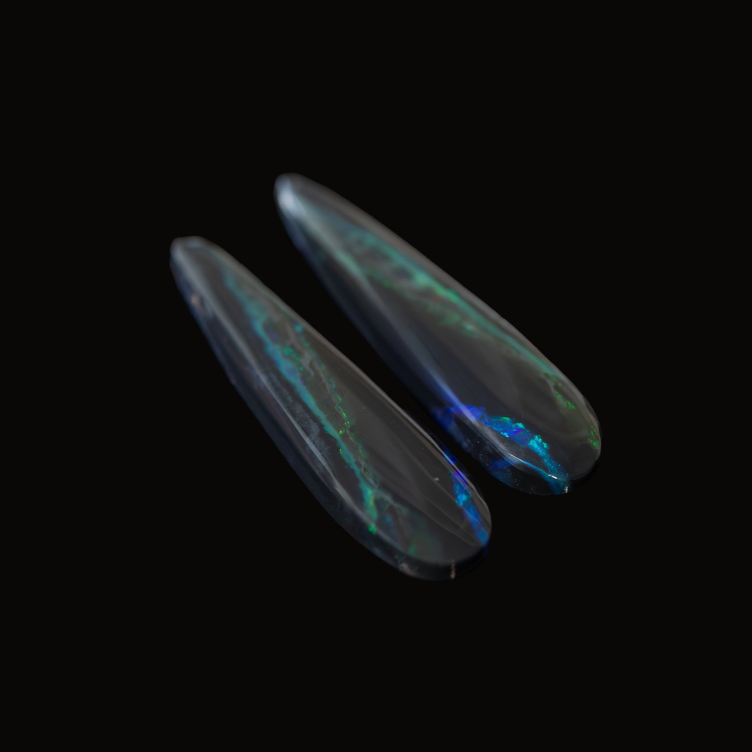 Two black opal stones with a play of colors on a black background