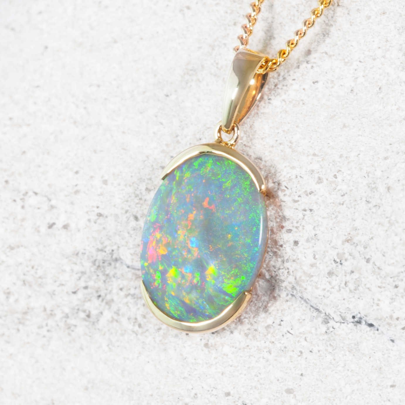 Black opal pendant on a gold chain against a textured white background