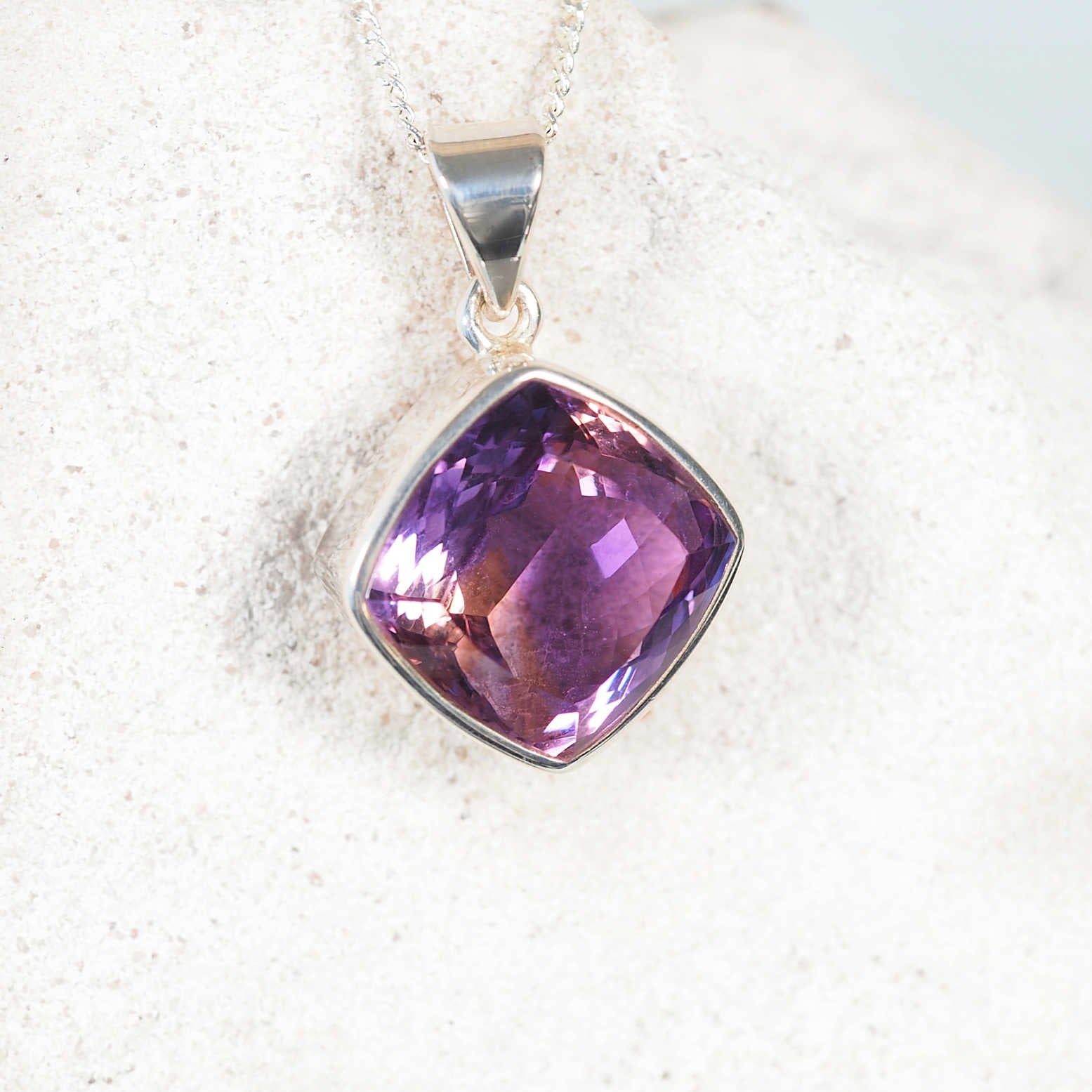 Faceted diamond-cut Amethyst pendant in silver bezel with radiant purple tones.