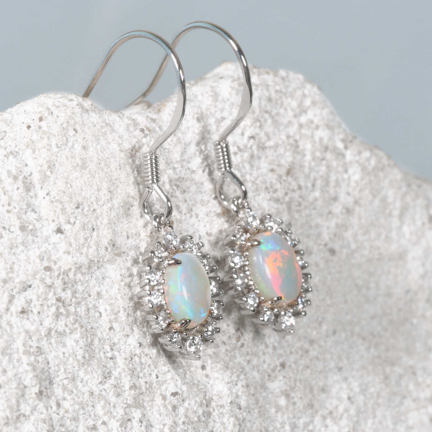 Opal earrings on a textured white surface with a light gray background