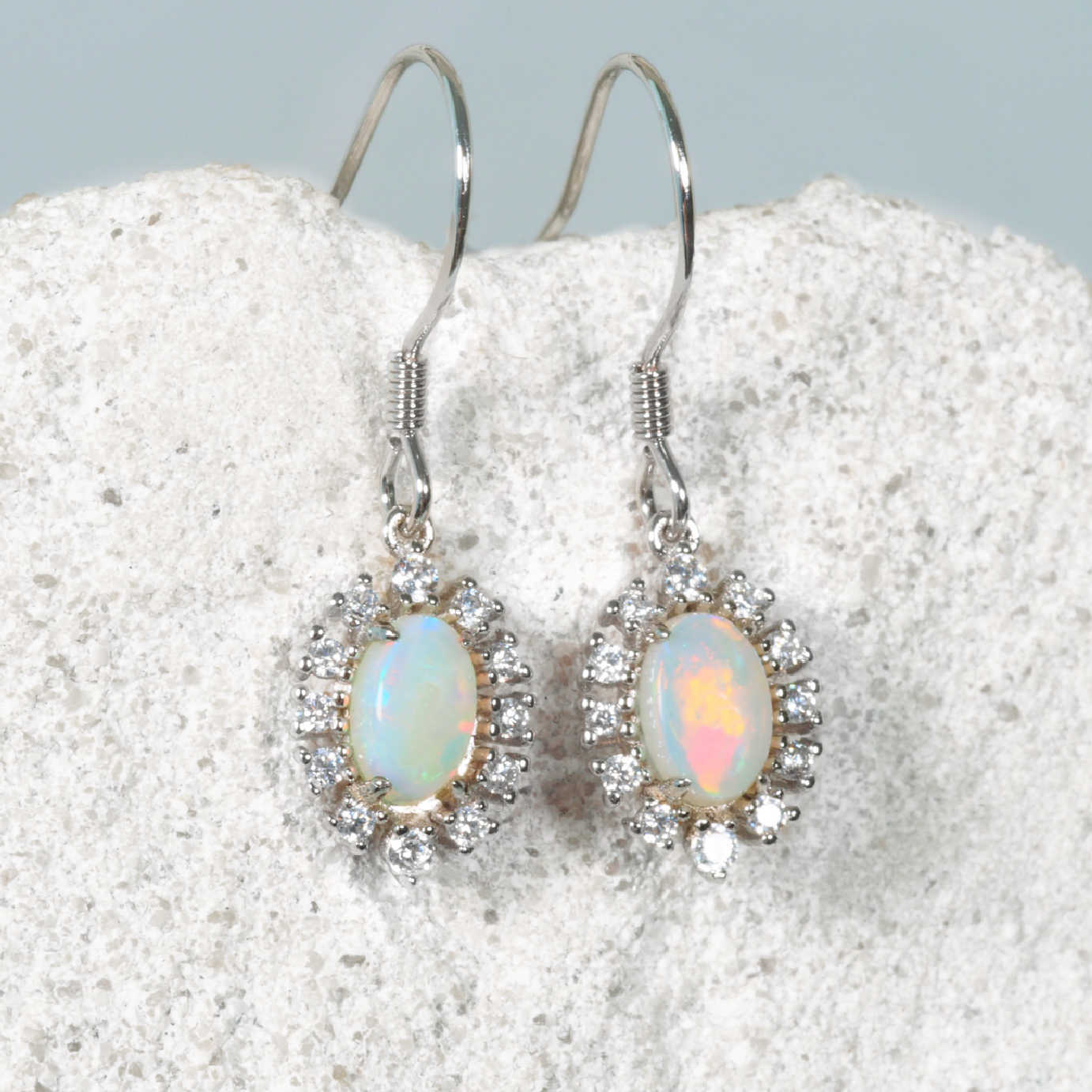 Opal earrings with silver hooks on a textured white surface