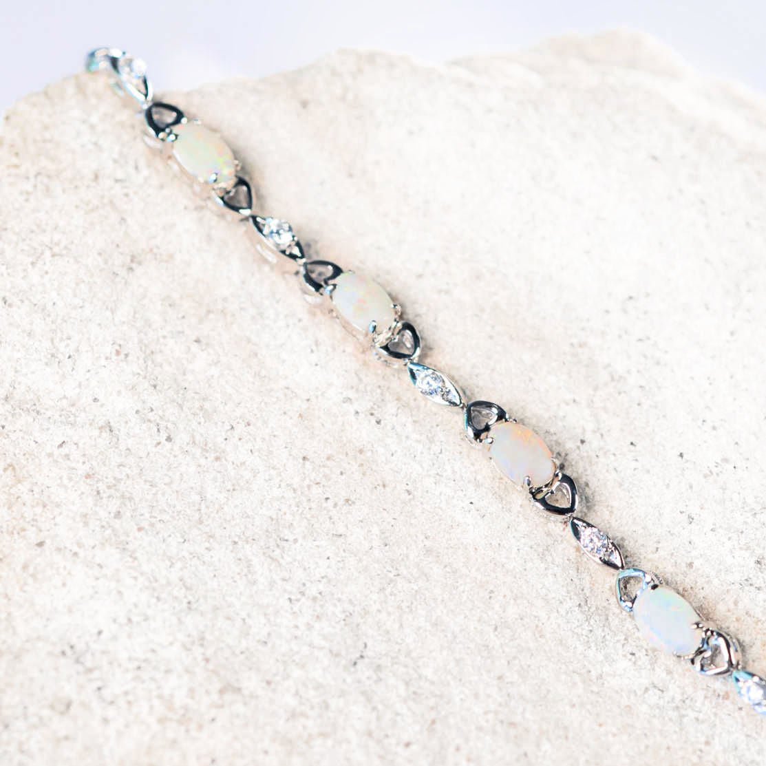 Silver bracelet with heart-shaped opal stones on a sandy background