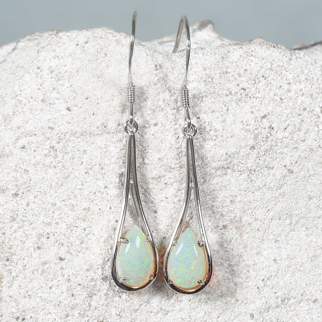 Teardrop-shaped green opal earrings on a textured stone surface