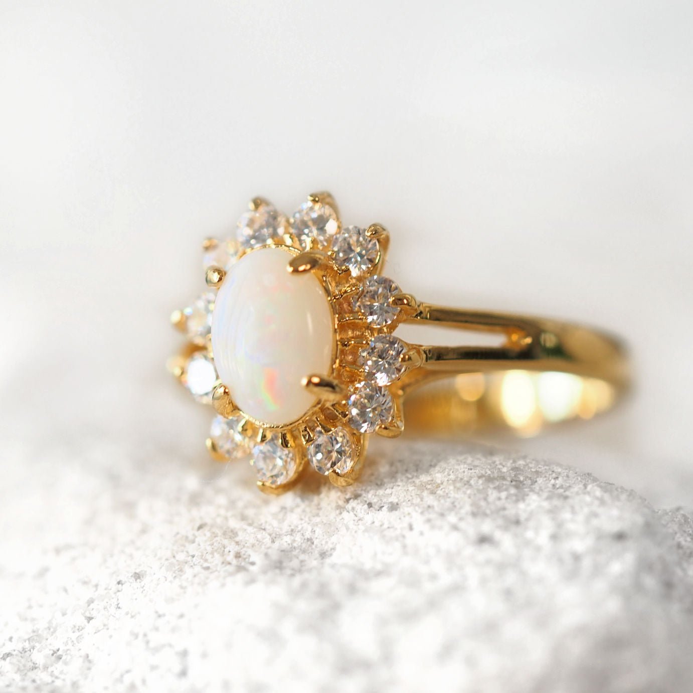 Gold ring with a central opal stone and diamond-like stones on a white background