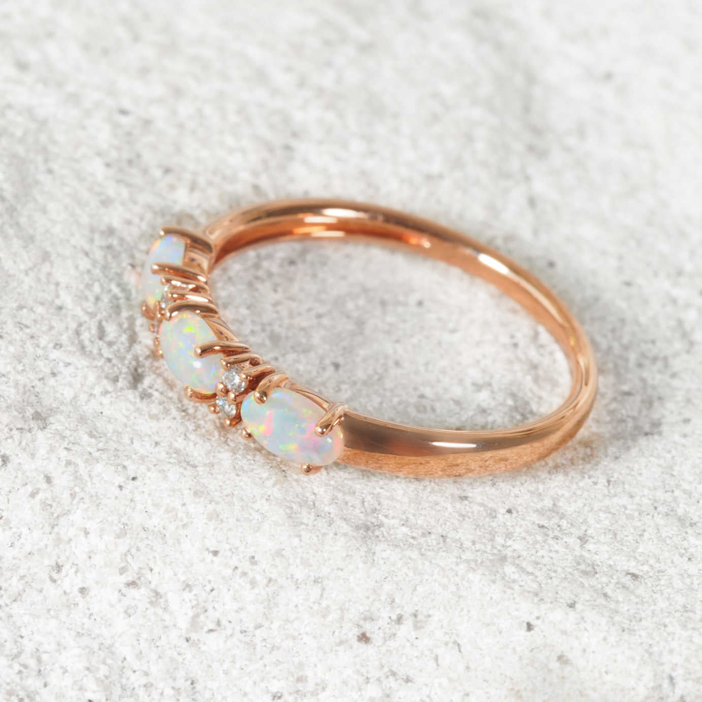 Rose gold ring with opal stones on a textured white background