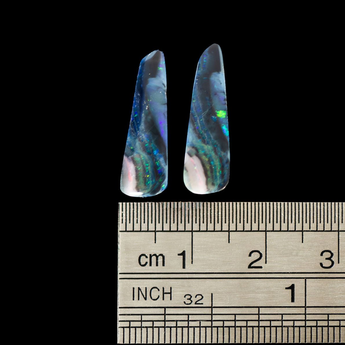 Two colorful opal stones with a ruler for scale on a black background