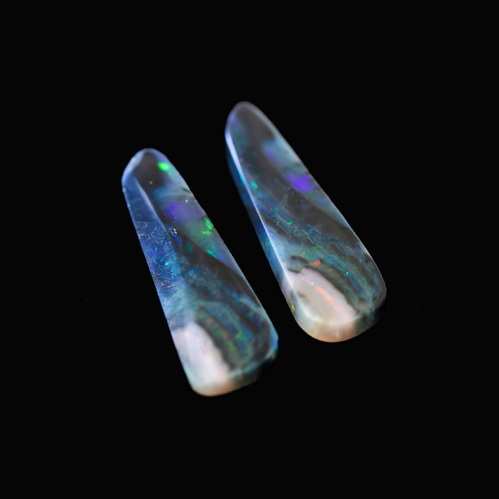 Two opal stones with multicolored fluorescence on a black background