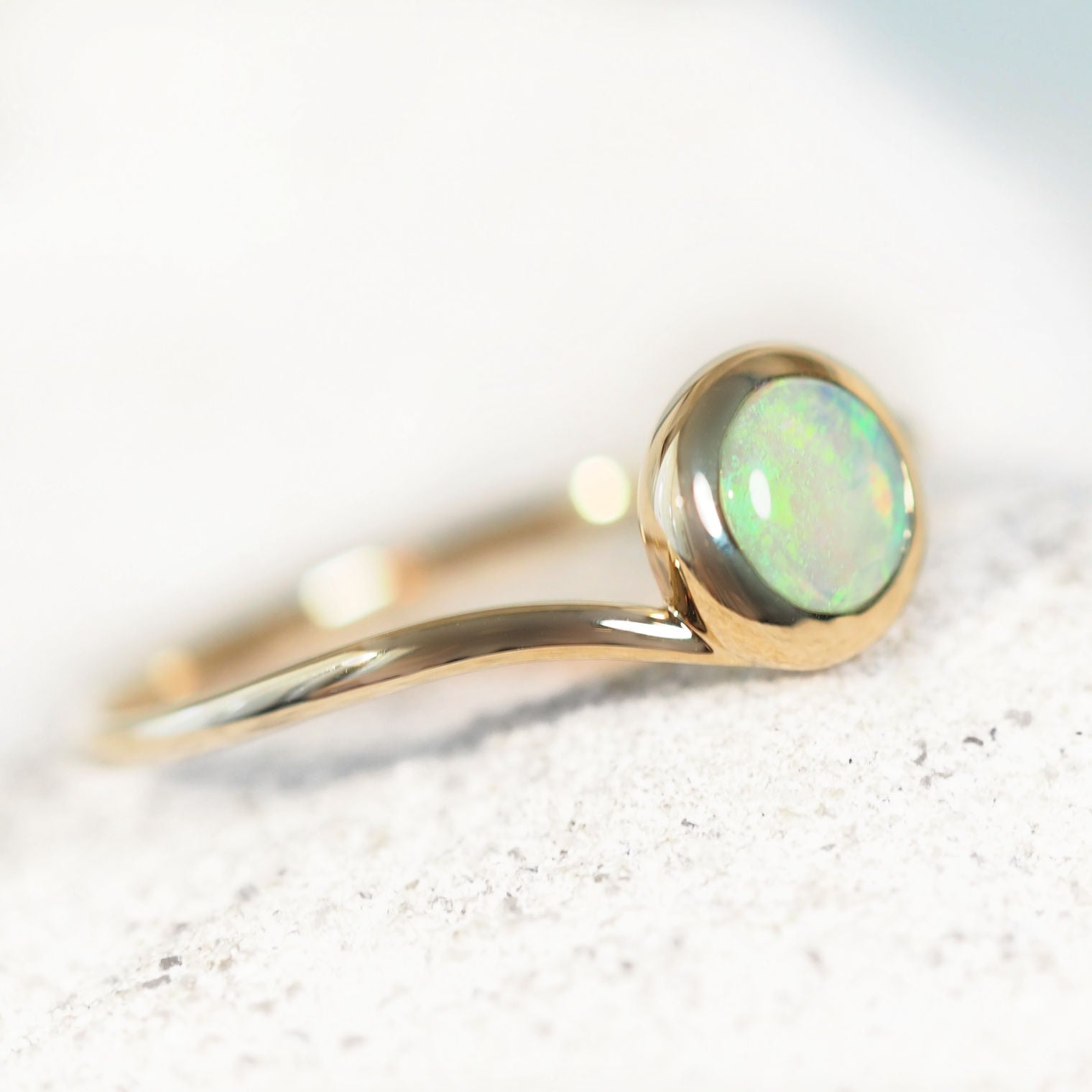Gold Lightning Ridge opal ring with a green opal stone on a light background