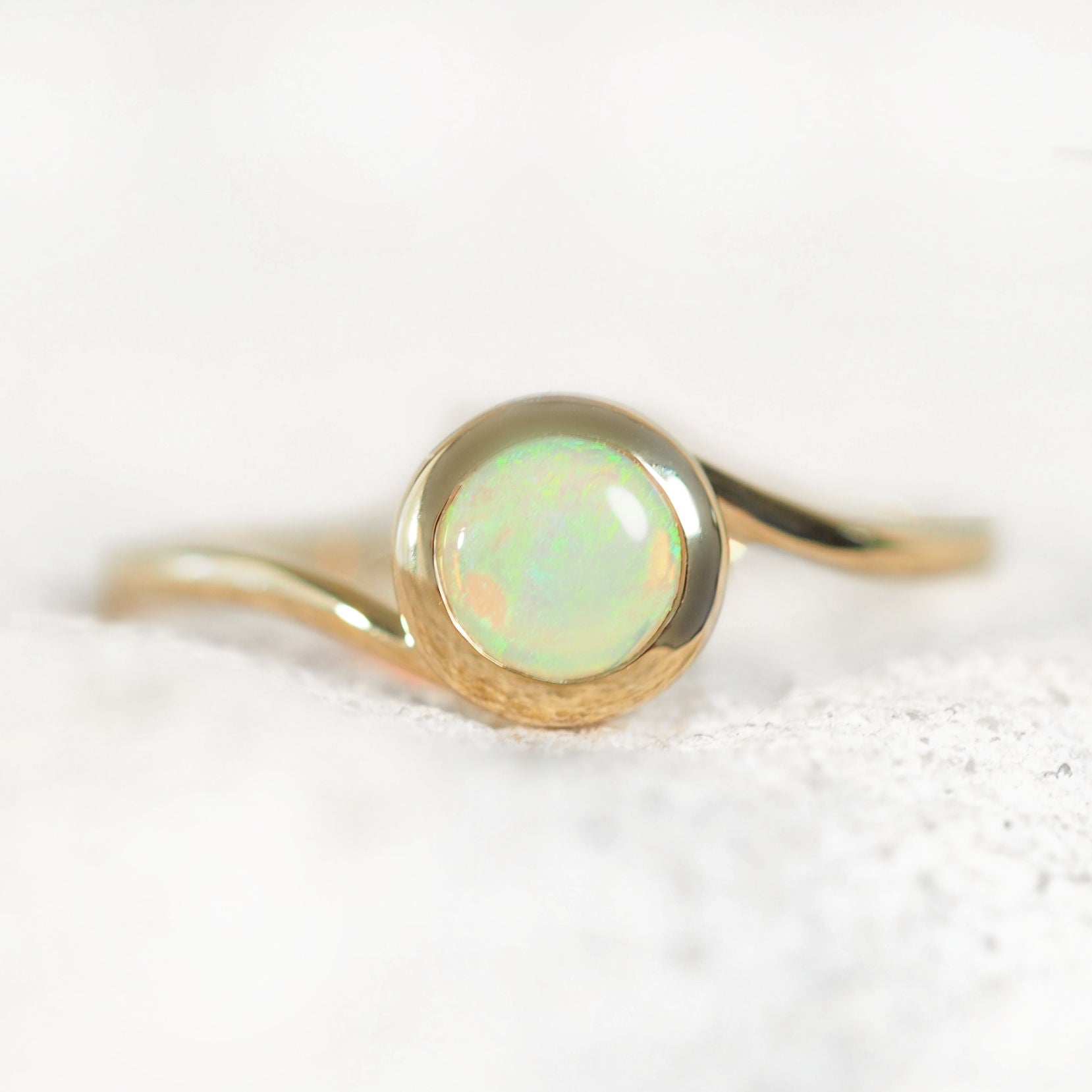 Australian gold ring with a green opal stone on a textured white surface