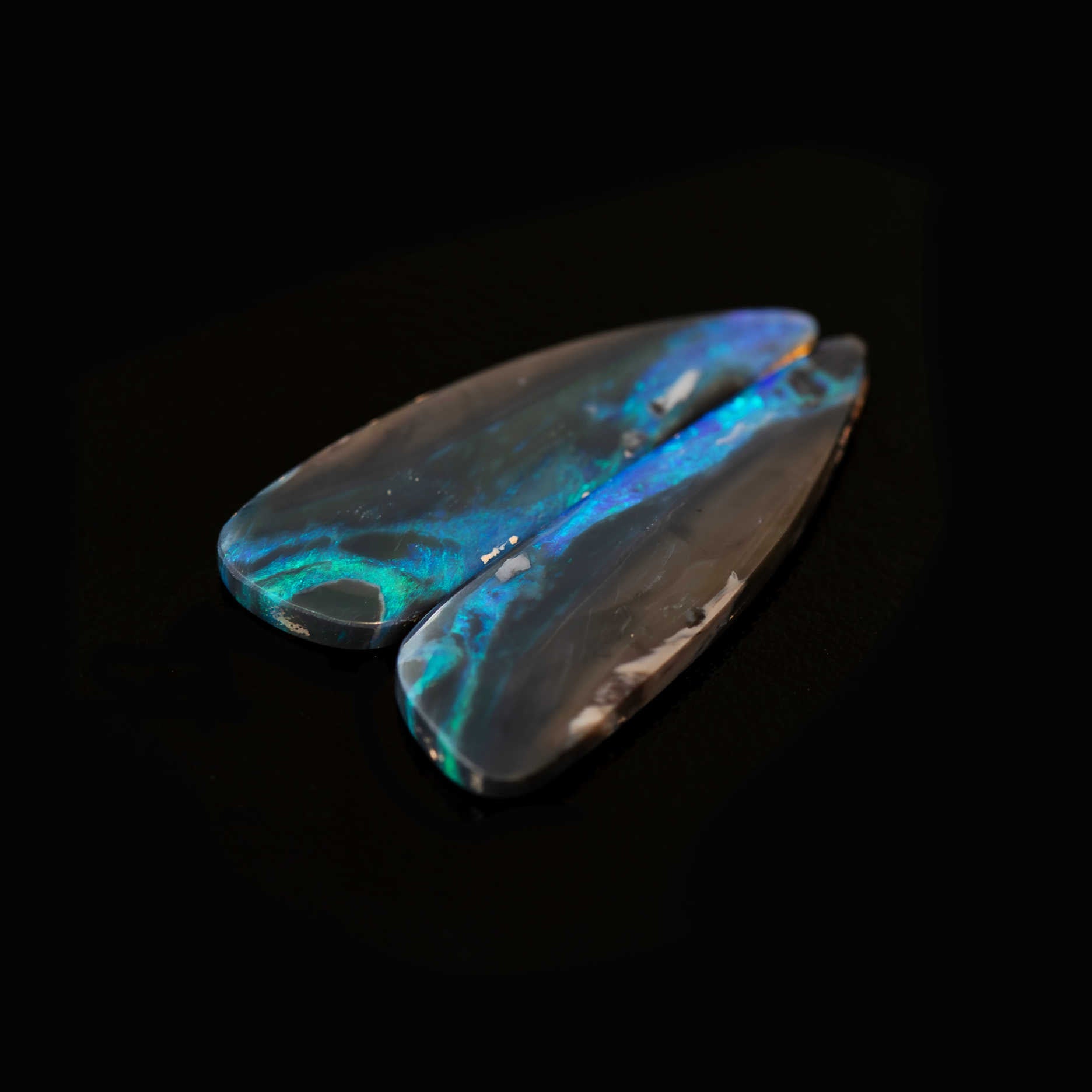 Two black opal stones with vibrant blue and green fluorescence on a black background