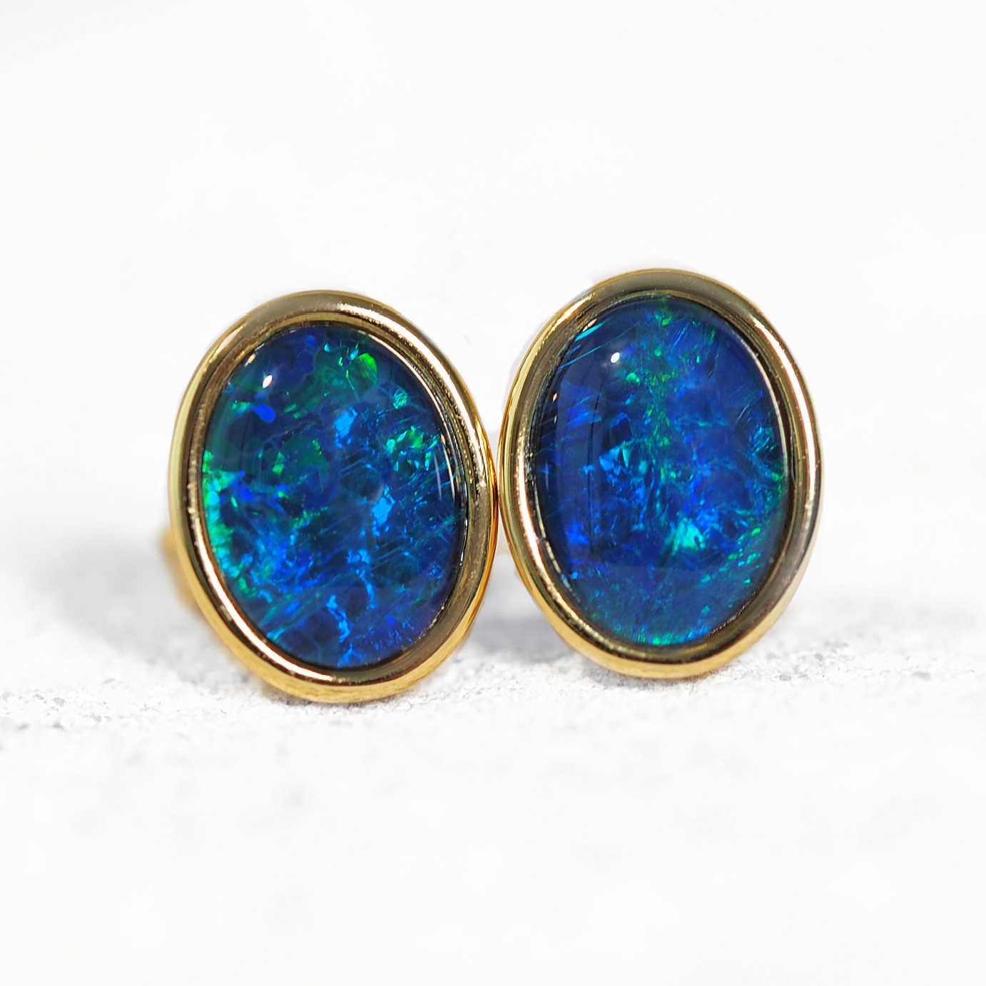 Pair of blue opal earrings with gold setting on a white background