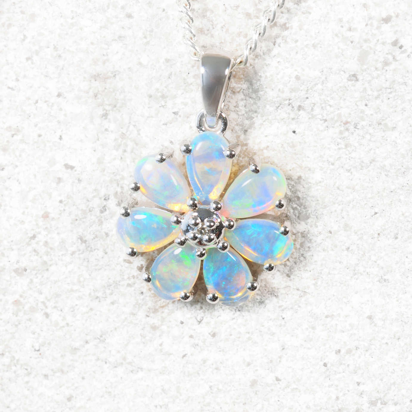 Opal flower pendant on a silver chain against a white background