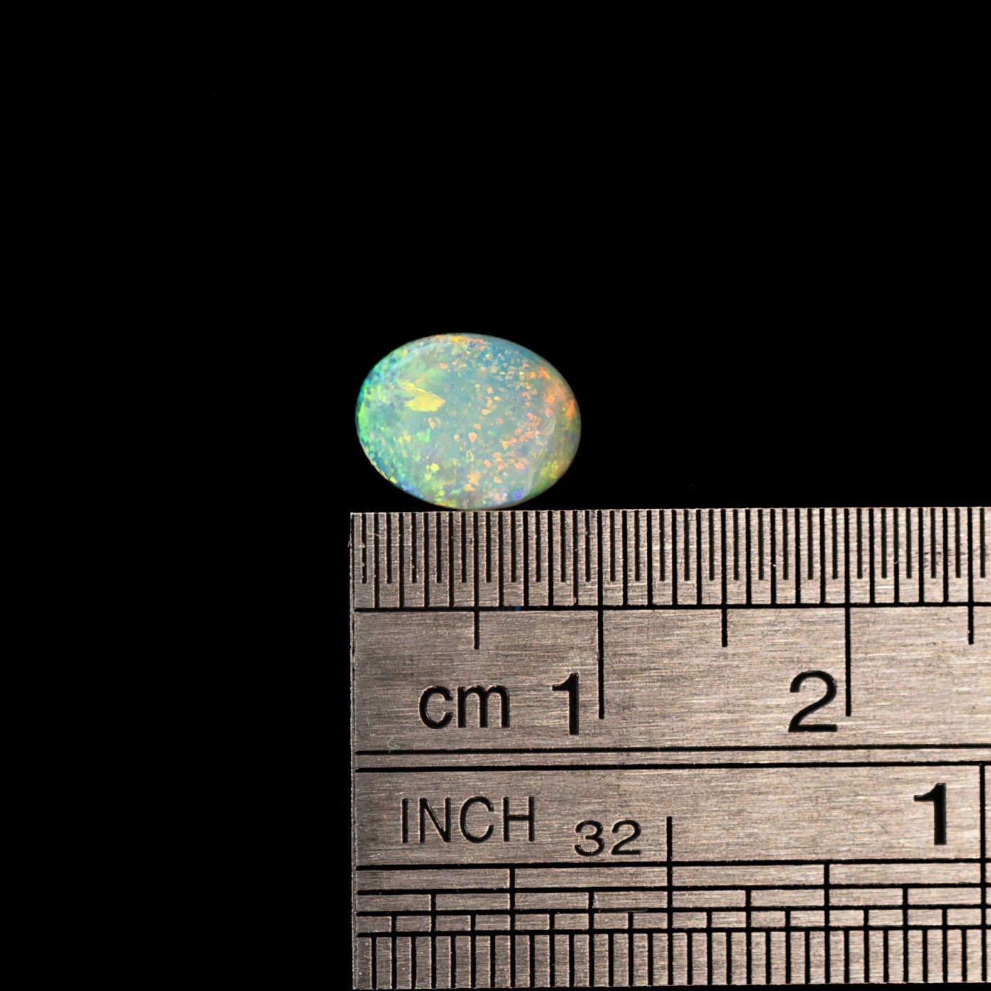 Opal stone on a ruler for size measurement against a black background