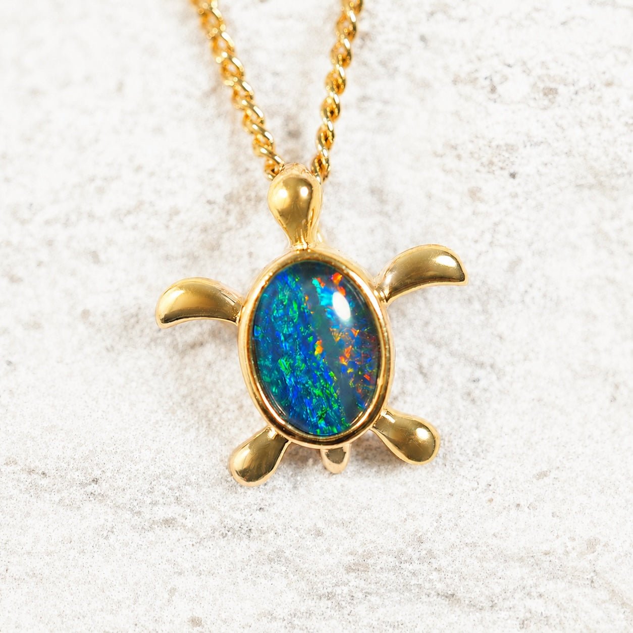 Gold turtle pendant with a colorful opal gemstone on a light background