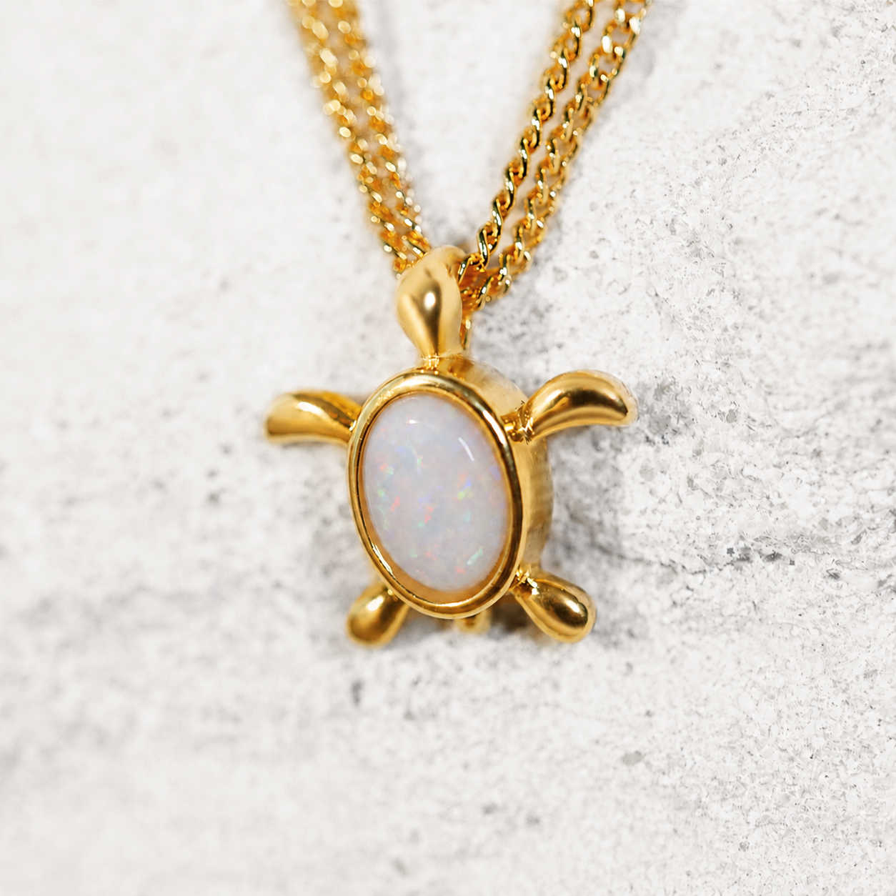 Gold turtle opal pendant necklace with a white stone on a textured surface